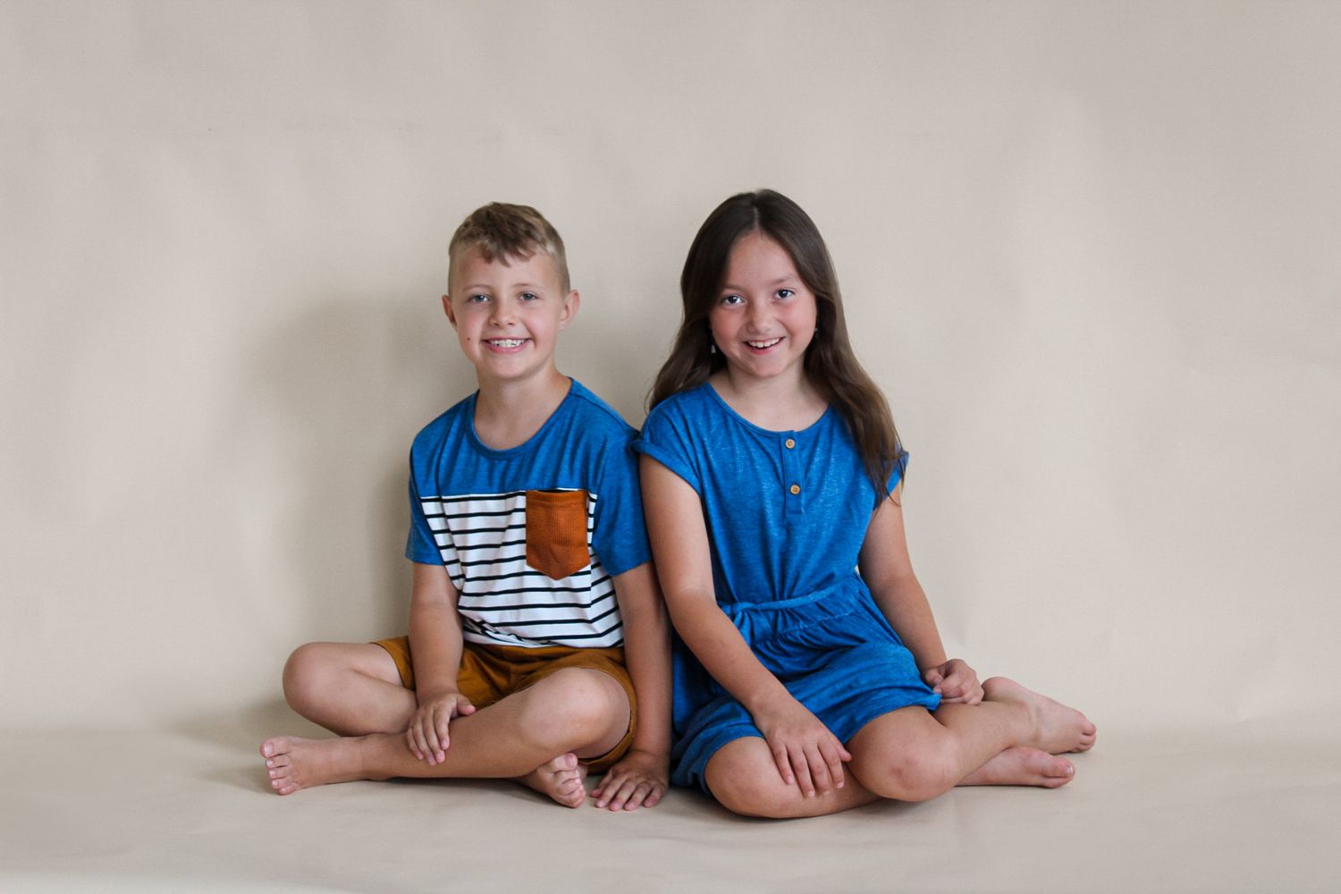 Siblings in casual clothing sitting together during studio photography session.