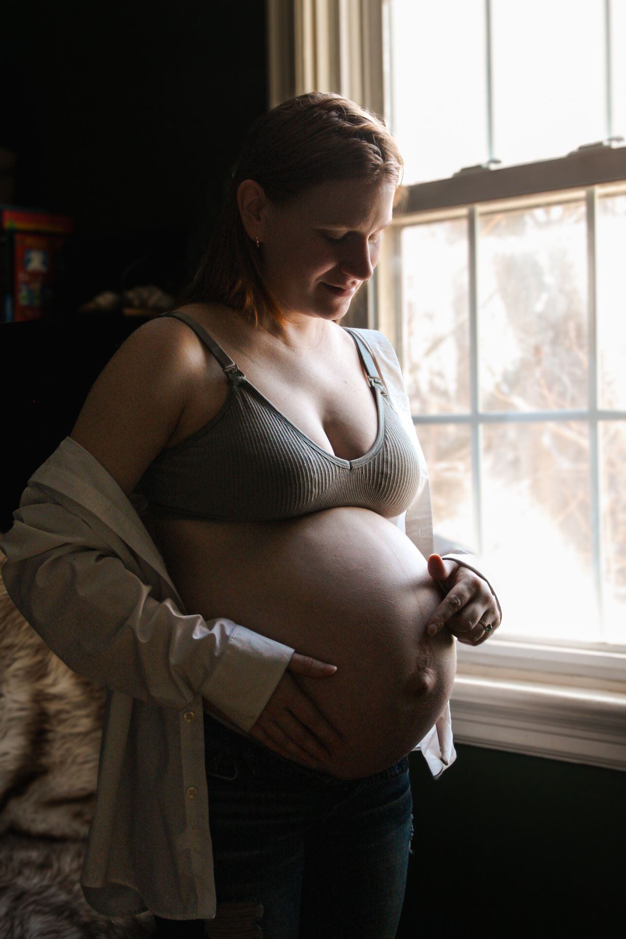 Side profile of pregnant belly near window in natural lighting.