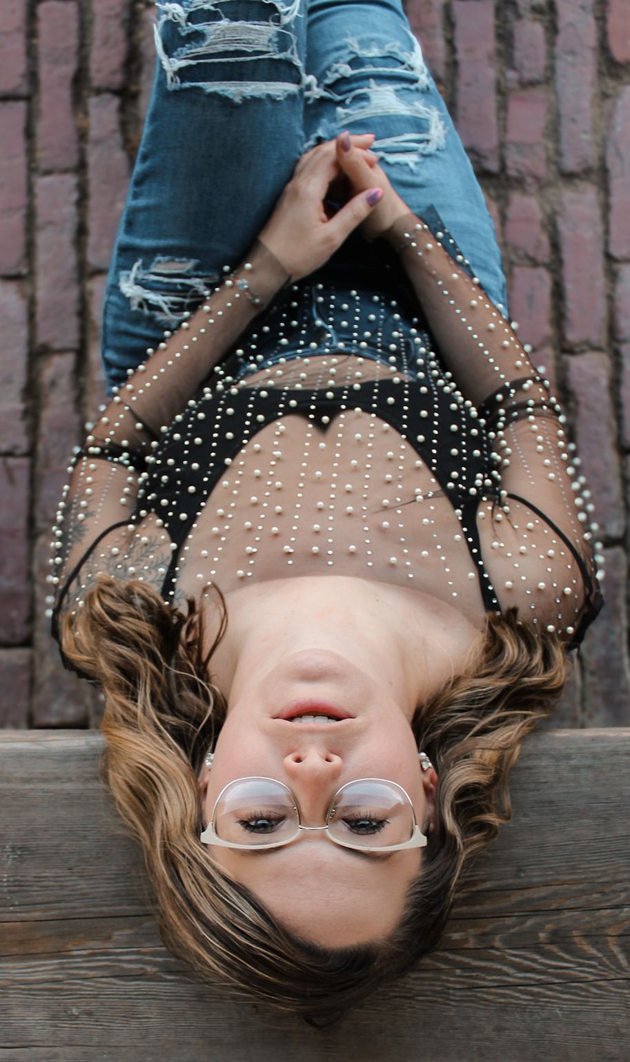 Creative overhead portrait featuring ripped jeans and sheer polka dot top on wooden surface.