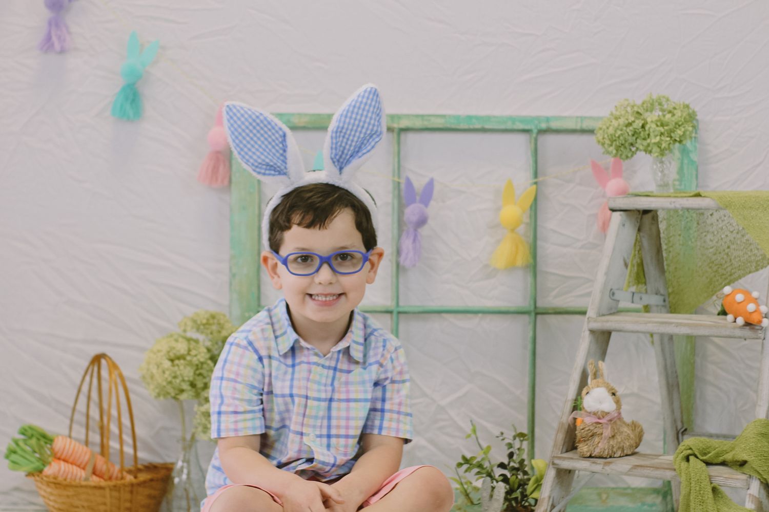 Easter-themed photo setup with pastel decorations and bunny ears against white backdrop.