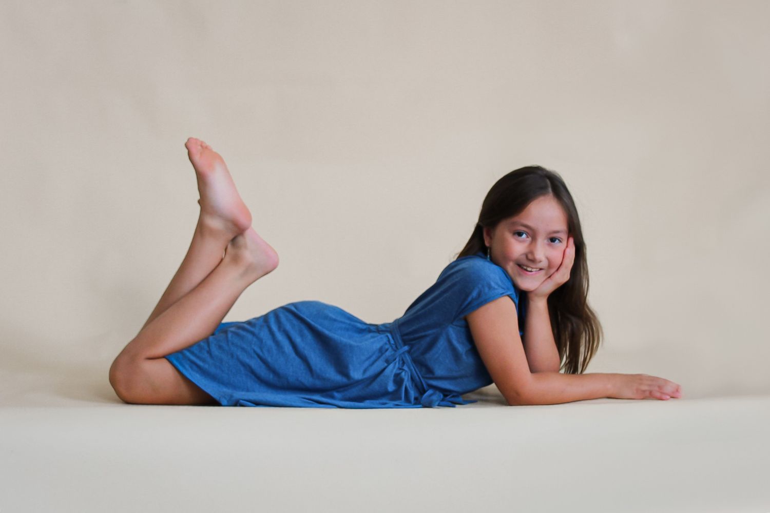 Person in blue dress lying down during minimalist studio photo session against neutral background.