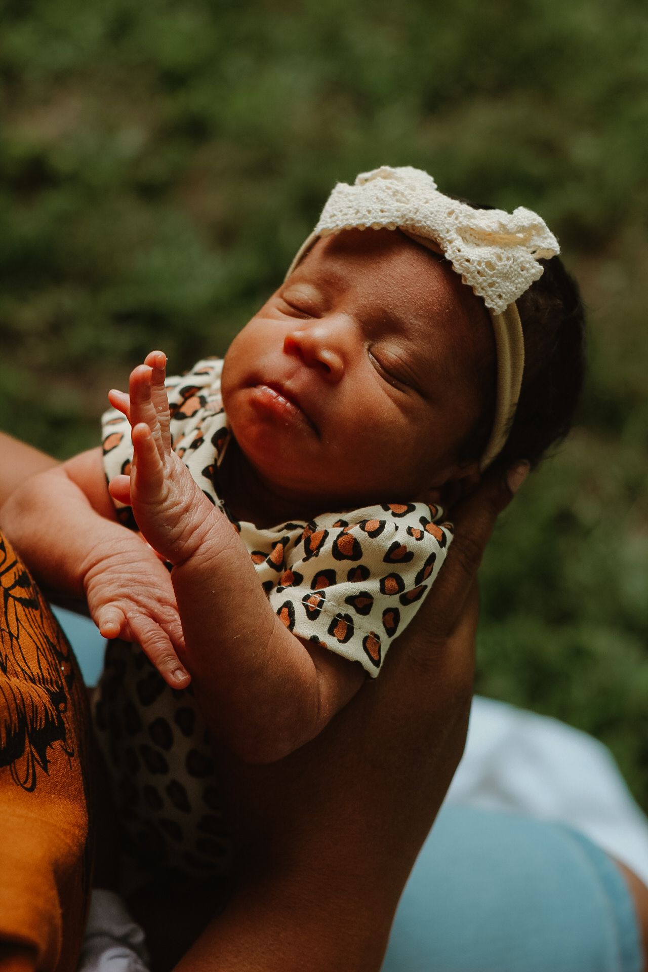A sleeping baby wearing a leopard print outfit and white headband rests peacefully against a blurred green background.