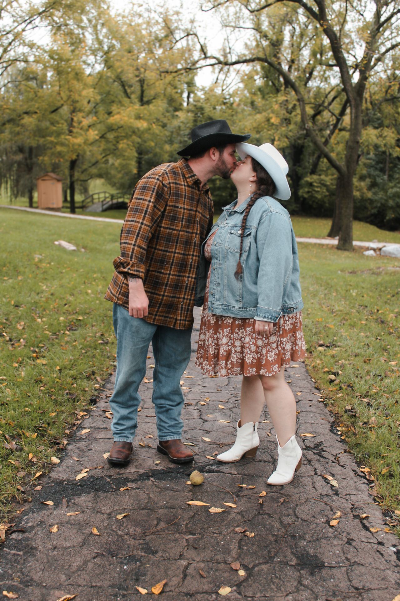 Couple in western wear sharing romantic moment on stone path surrounded by autumn trees.