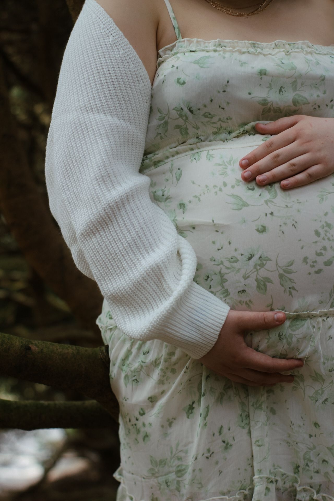 Close-up of hands cradling a pregnant belly in a delicate floral dress.