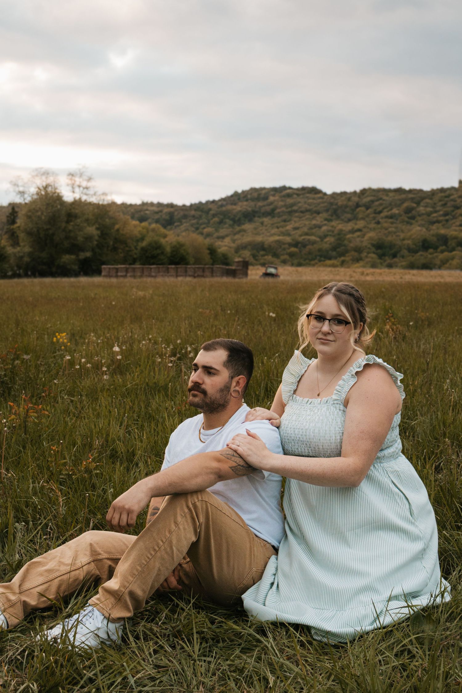 Couple sitting in a meadow field, man in white tee and tan pants, woman in mint dress wearing glasses.