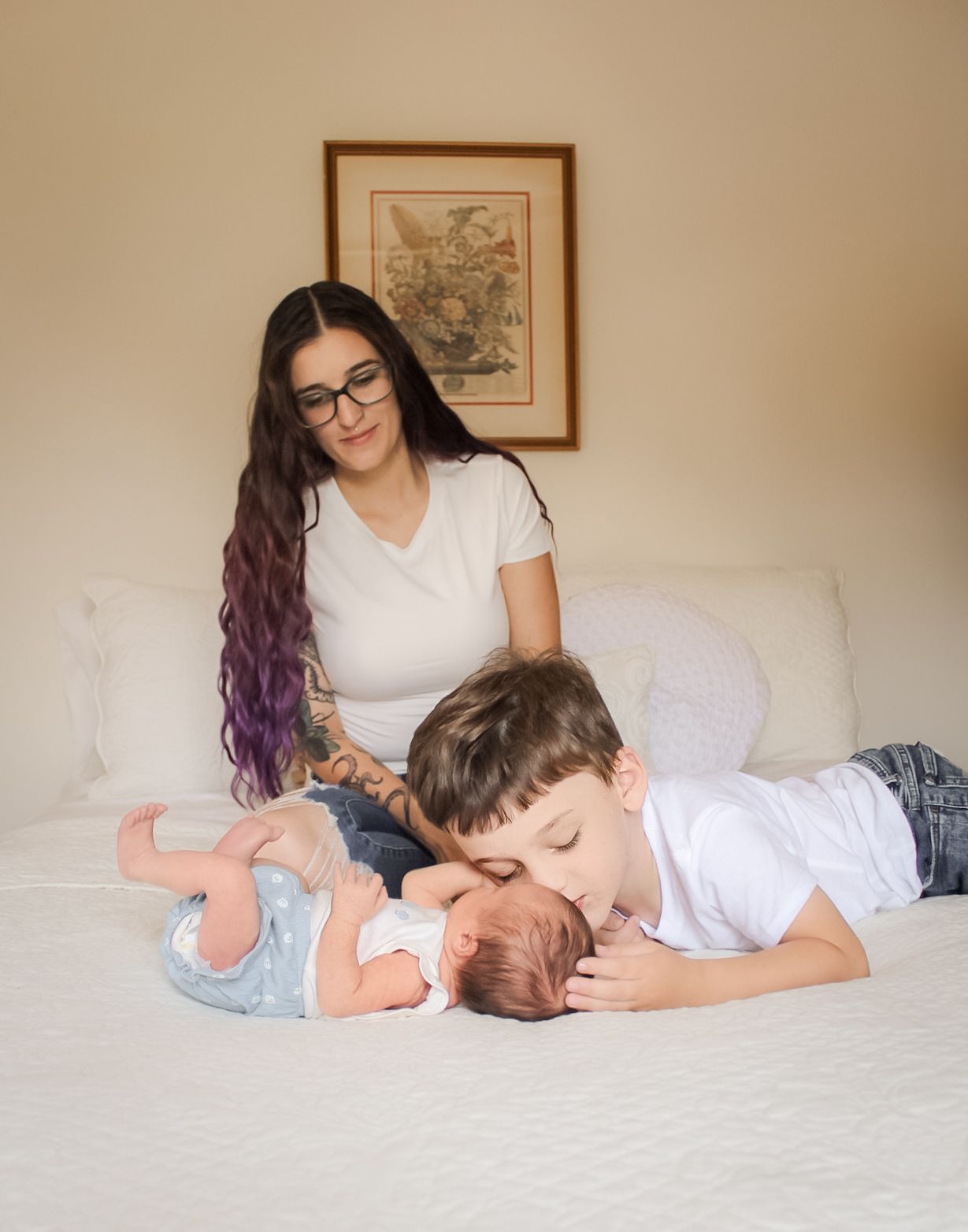 Tender moment shared while resting together on a white bedspread with framed artwork on the wall.