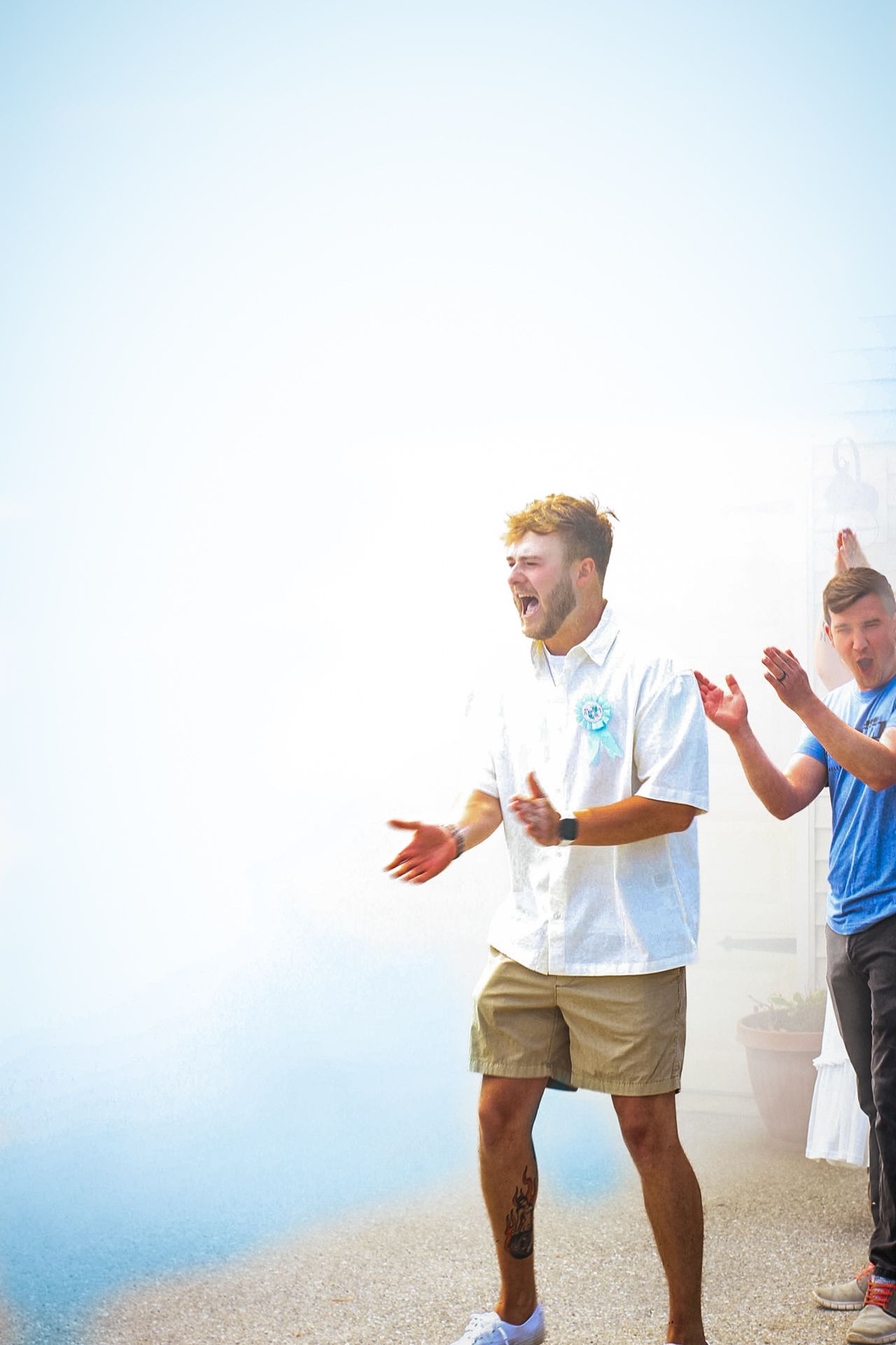 Group gathered outdoors celebrating with blue smoke effects in bright sunlight.