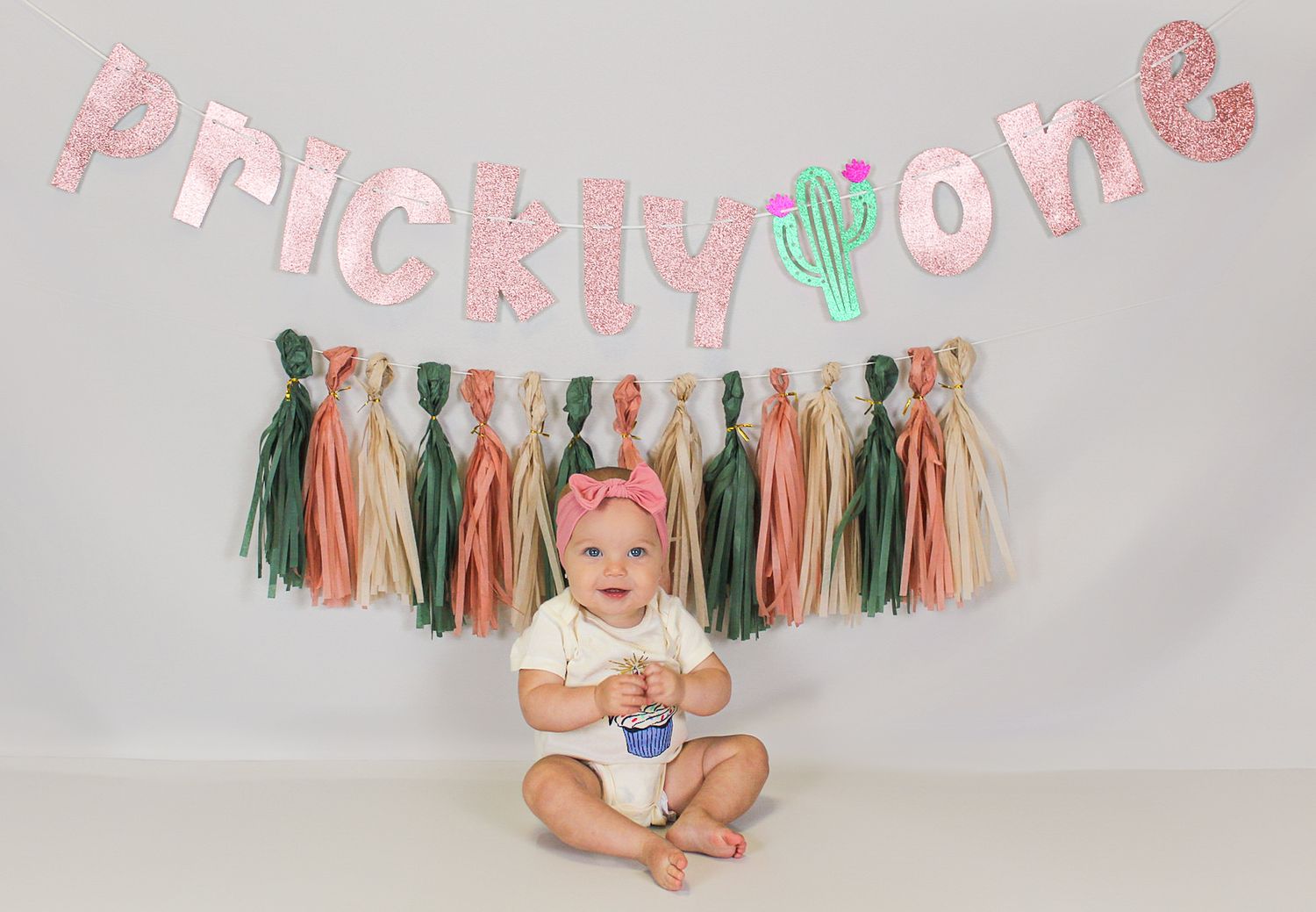Boho-style cake smash setup with pink and green tassels and 'Prickly One' banner.