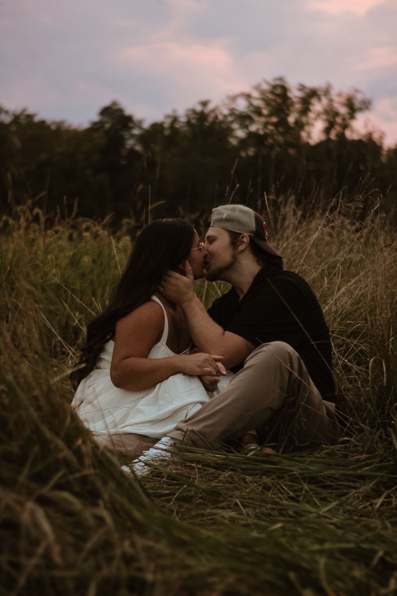A couple shares an intimate kiss while lying in tall grass during golden hour.