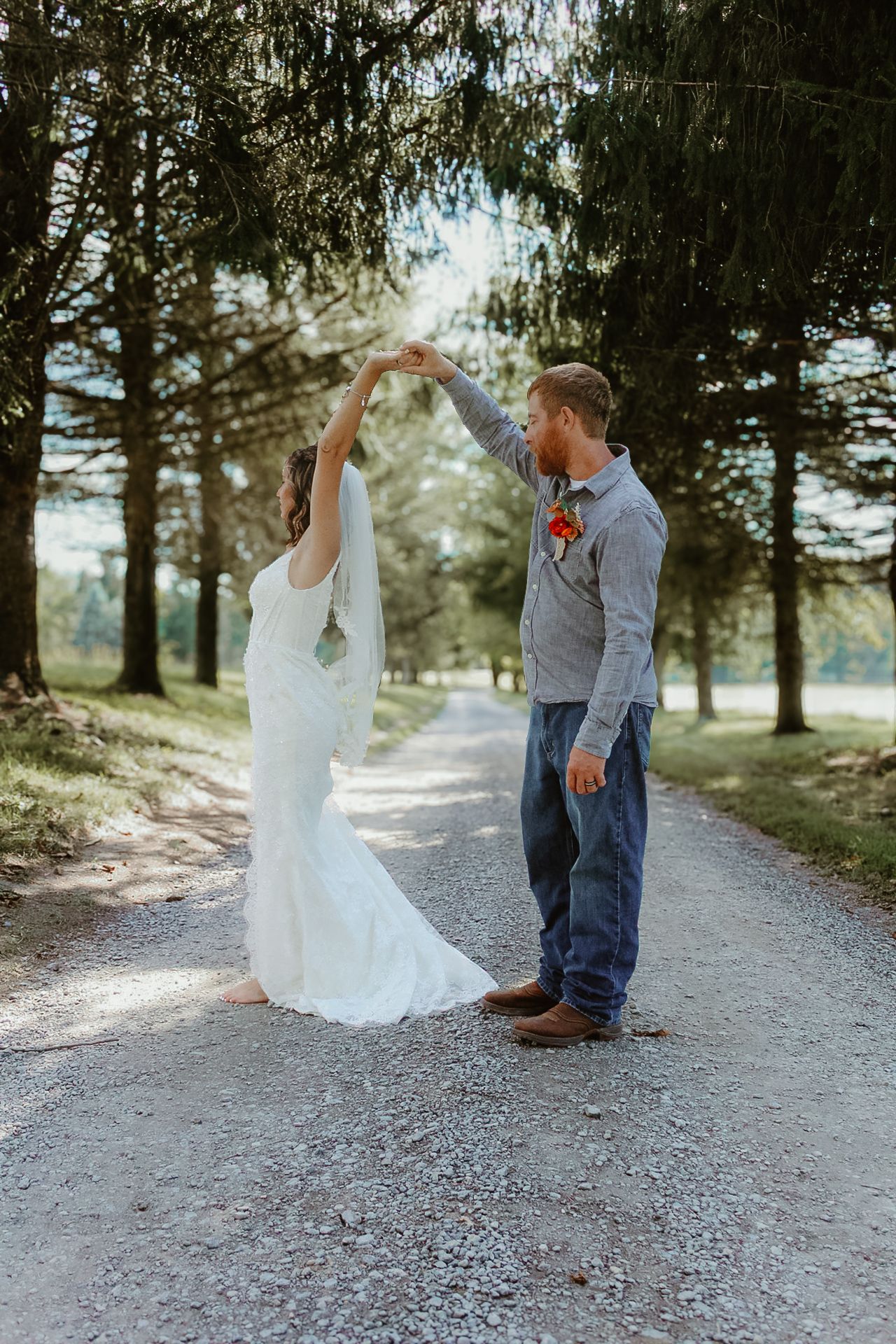 A couple shares a romantic moment on a tree-lined gravel path during their wedding photoshoot.