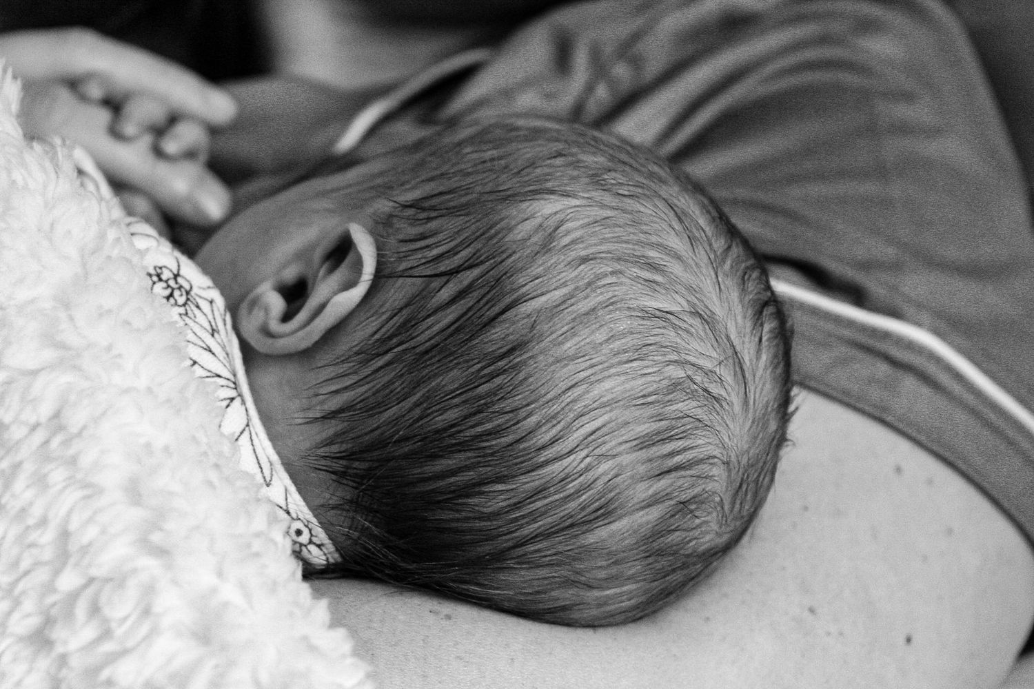 Black and white profile view of a newborn baby's head resting on soft fabric.