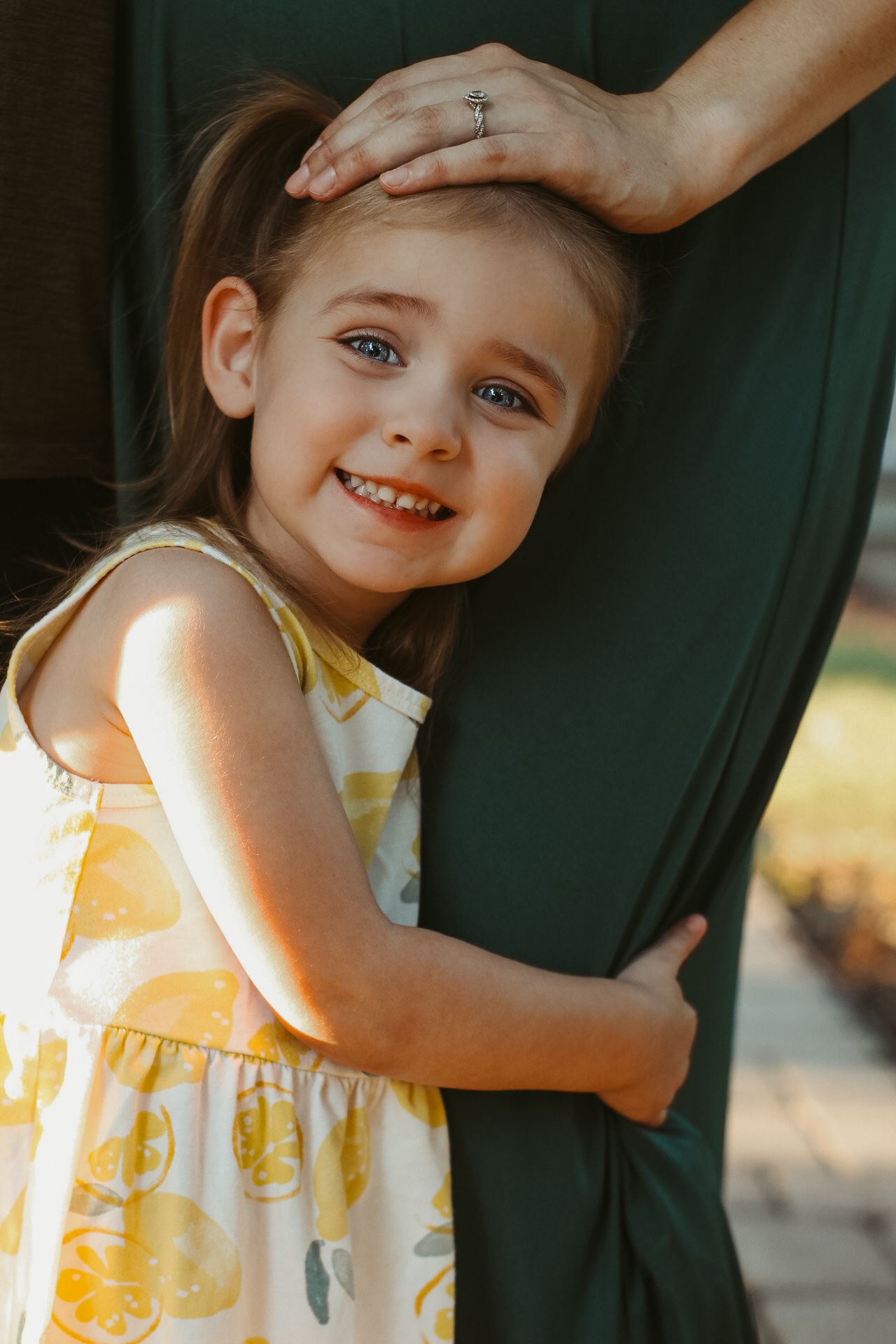 Young child in yellow and white floral dress playing outdoors in natural sunlight.