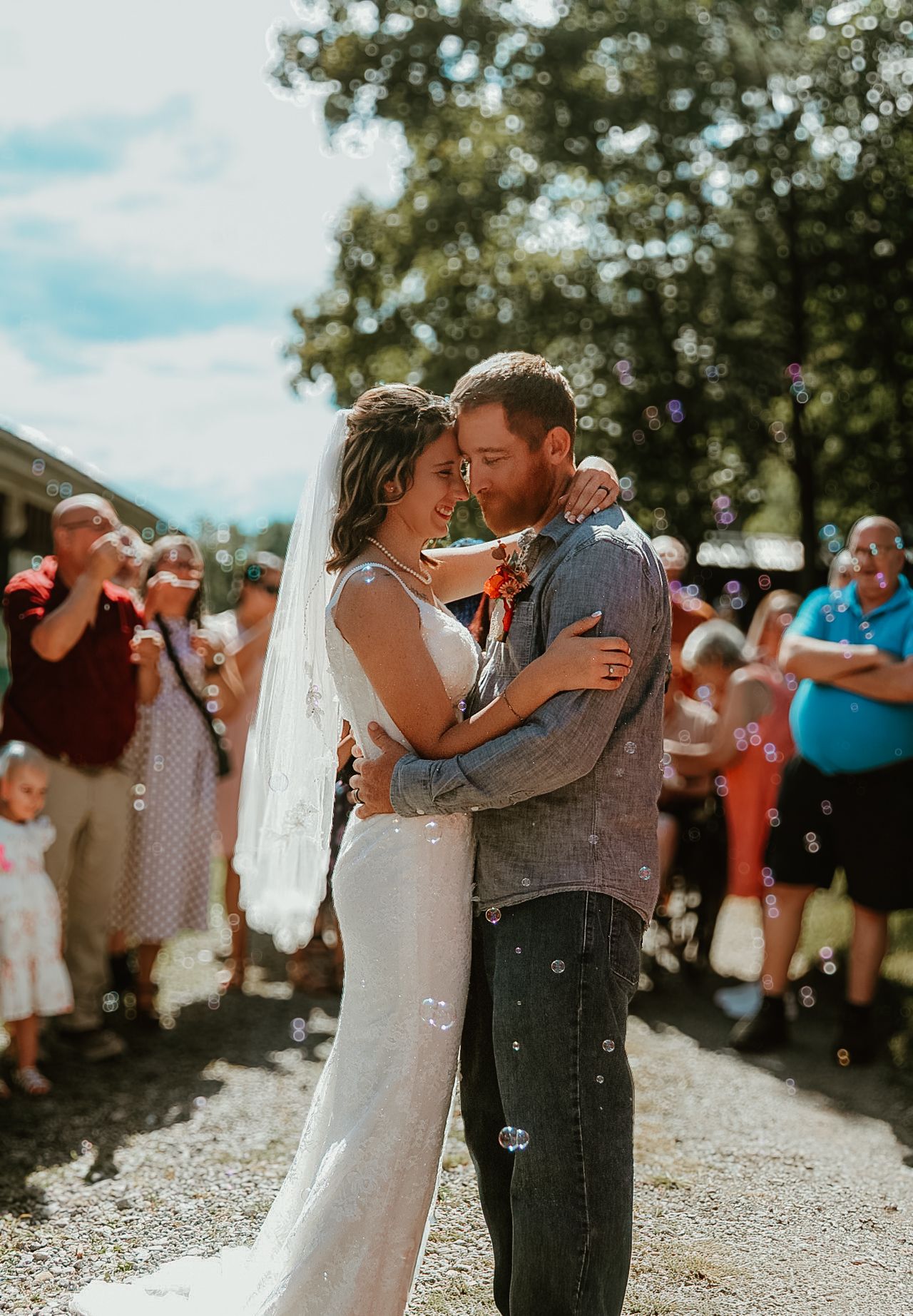 Newlyweds share a romantic first dance outdoors surrounded by wedding guests on a sunny summer day.