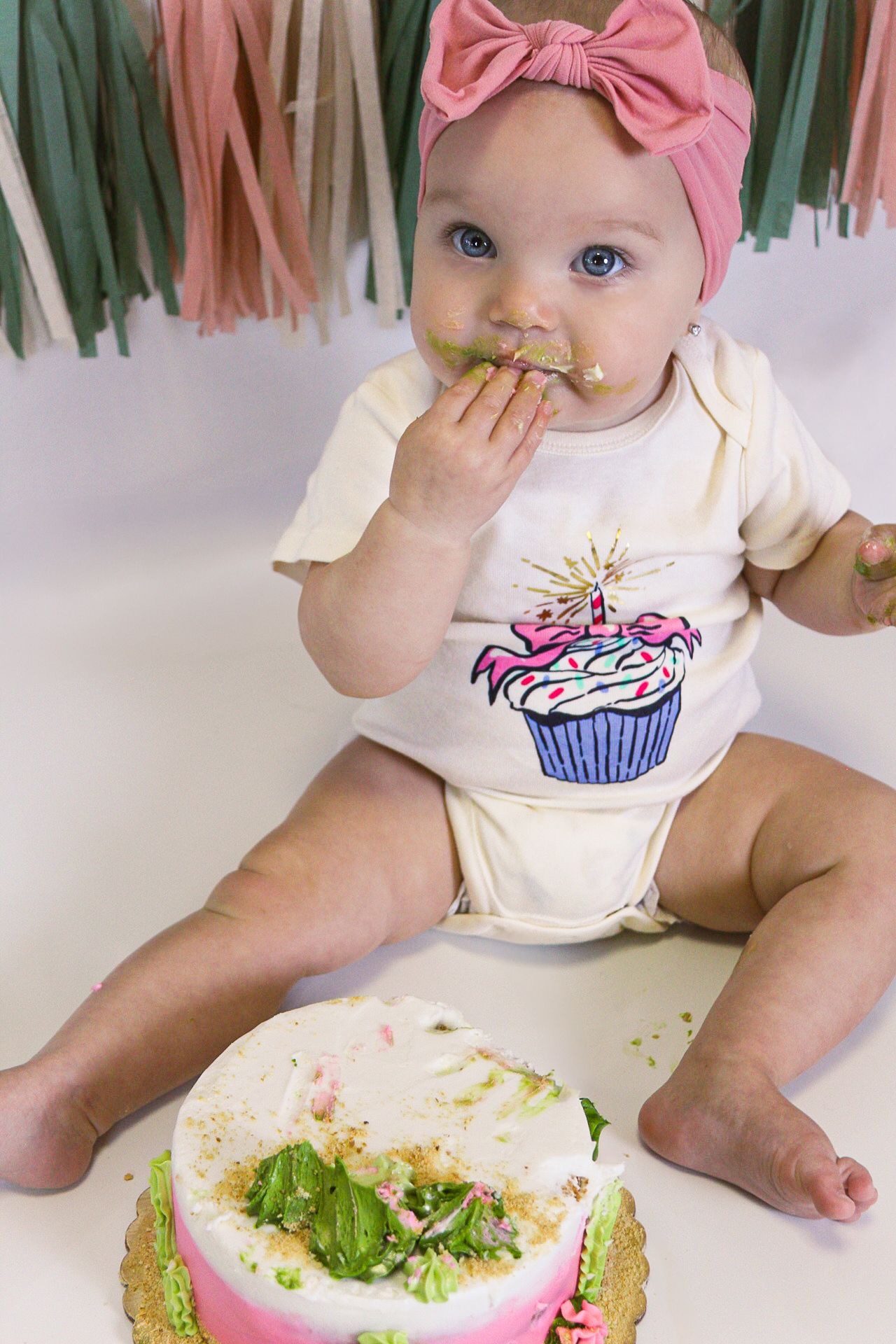 Cake smash photo with cupcake-themed outfit and demolished birthday cake.