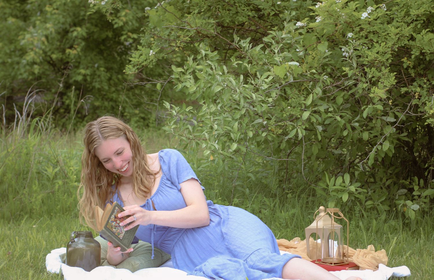 Woman in a blue dress enjoys a picnic on a white blanket with lanterns and old vintage books. Cottage Core vibes