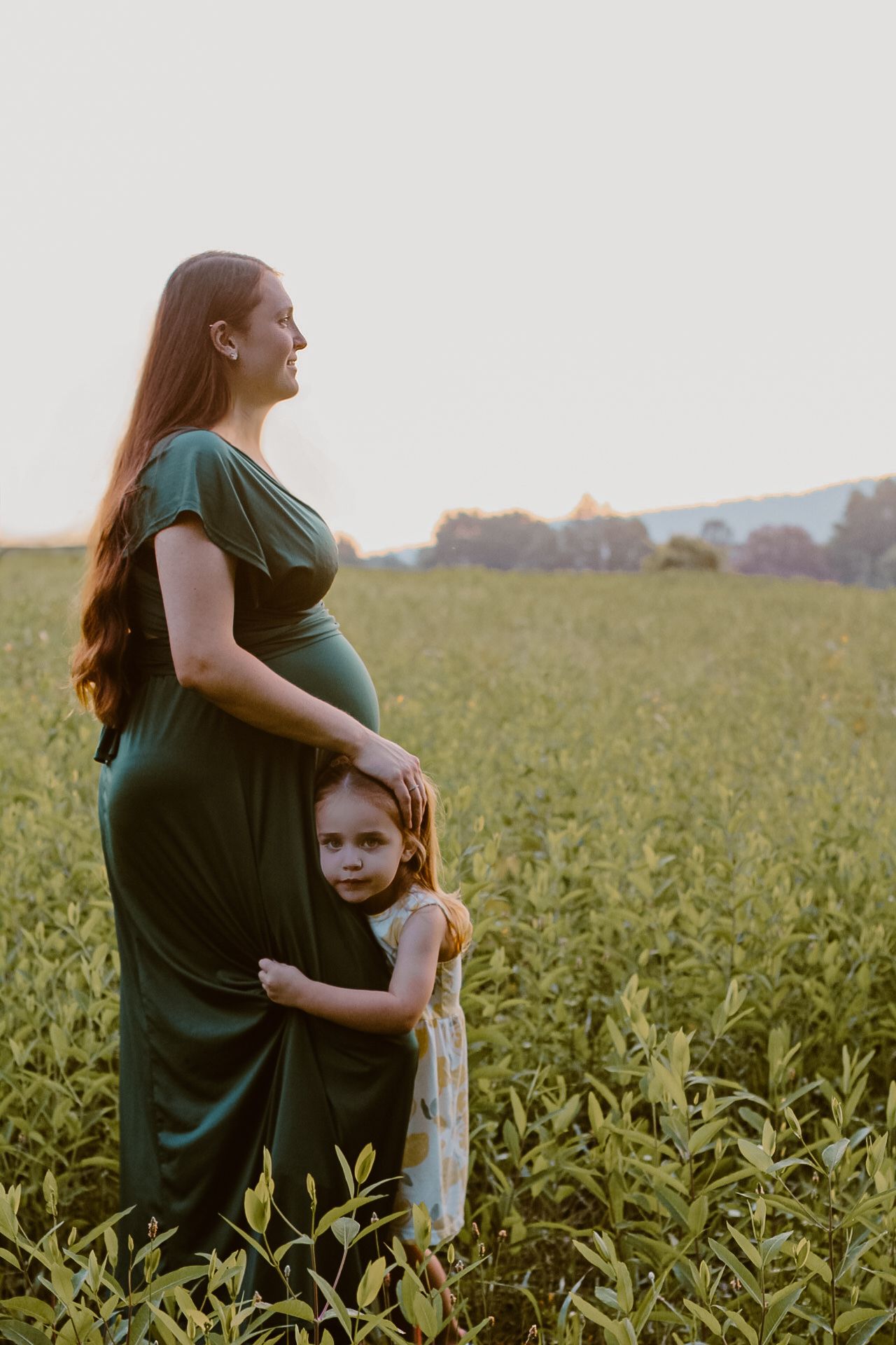 A mother in a green dress stands in a field while being hugged.