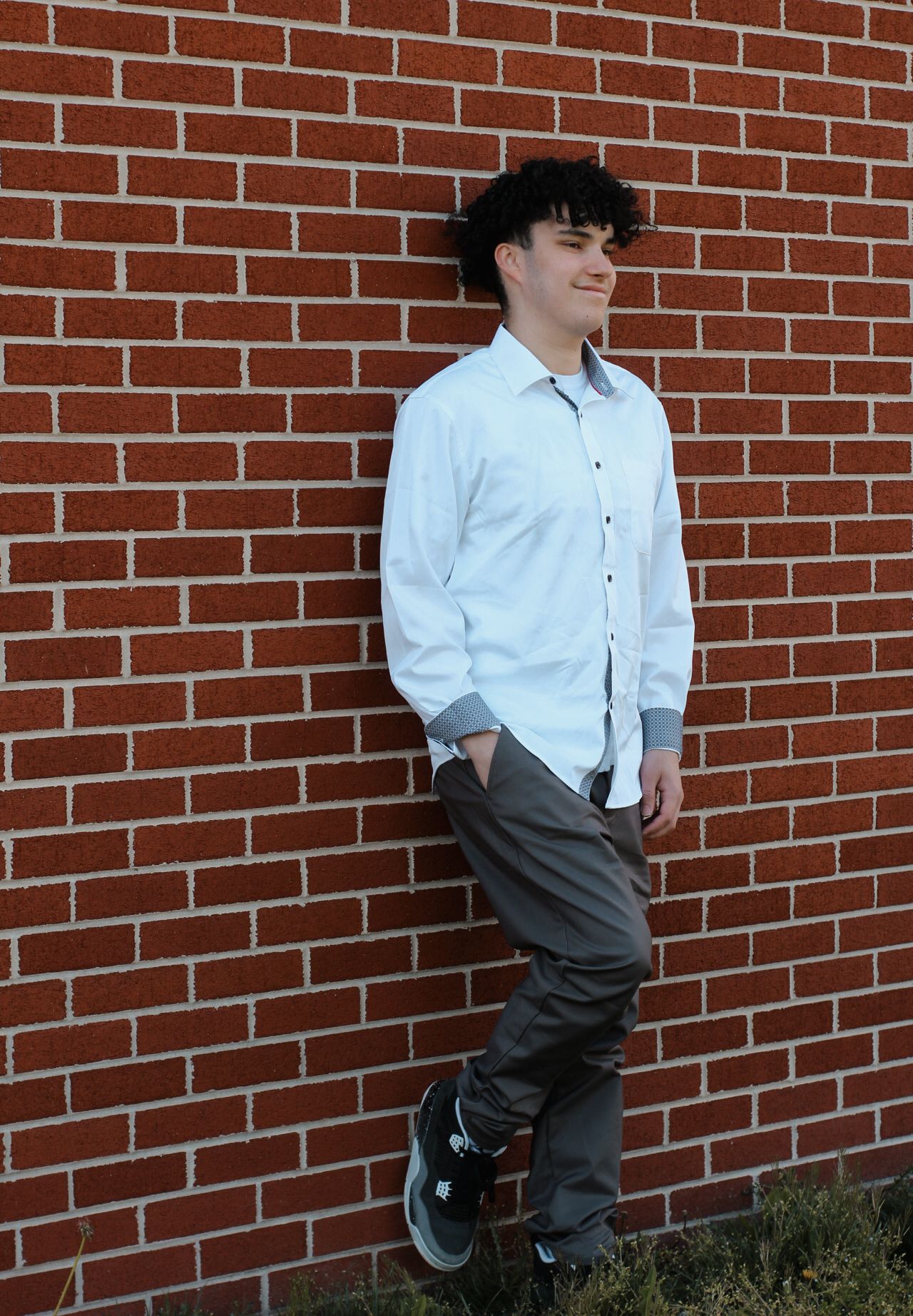 Casual portrait against red brick wall wearing white button-up shirt and grey pants.