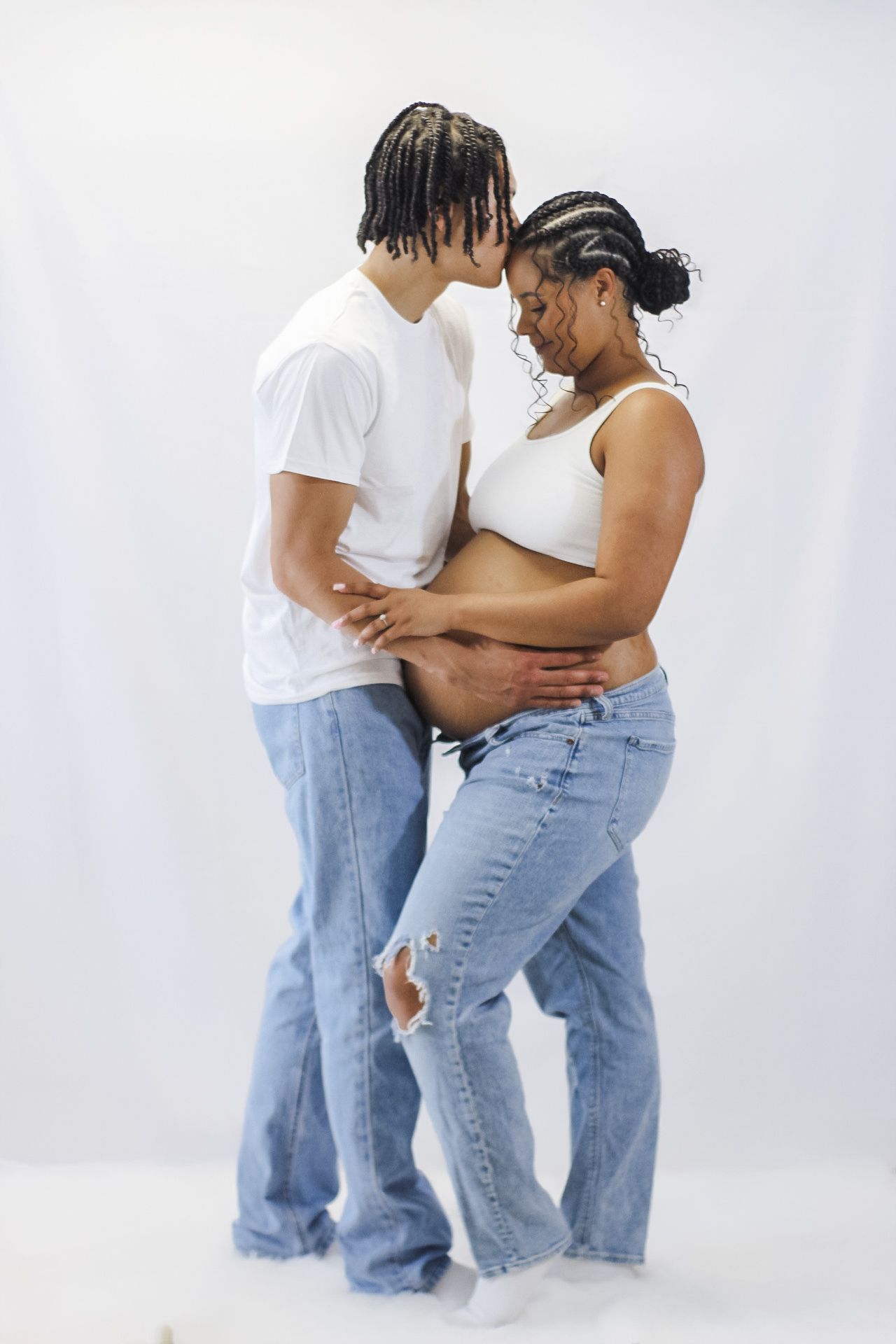 Intimate portrait of expecting couple in white and denim sharing tender moment.