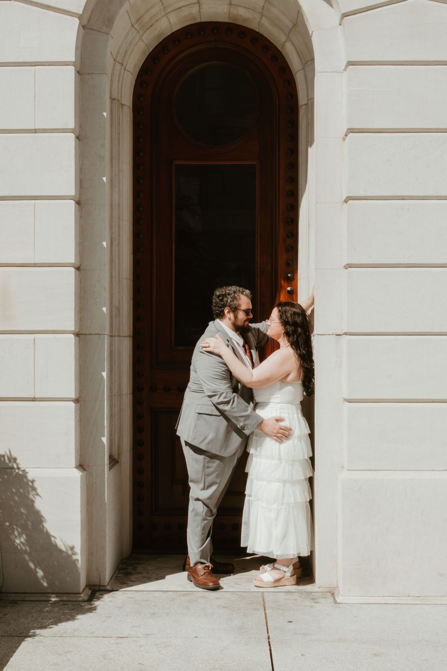 Couple sharing a romantic kiss in wedding attire outside an elegant arched doorway of a classic building.