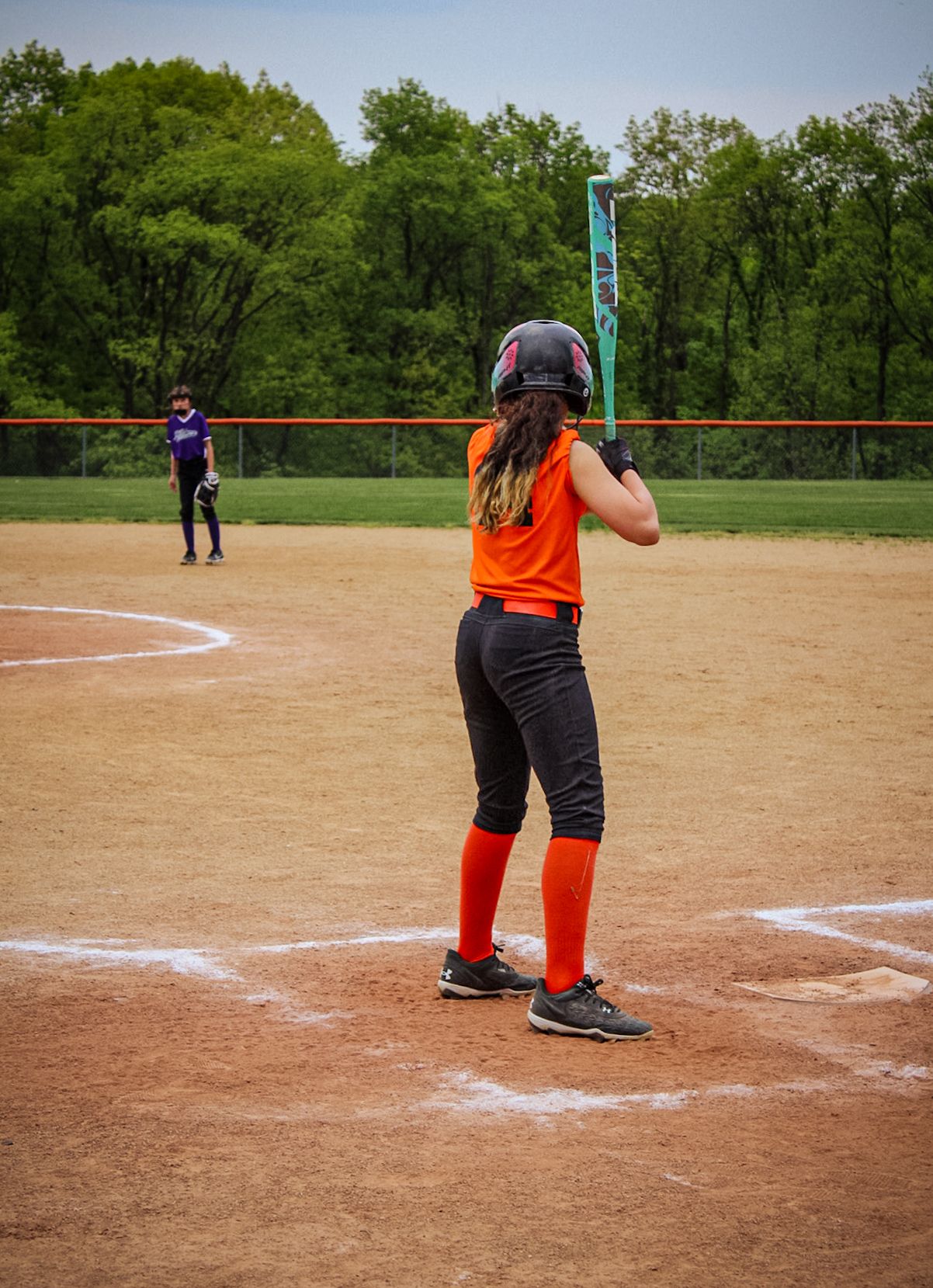 Softball player in bright orange uniform preparing to bat at home plate.
