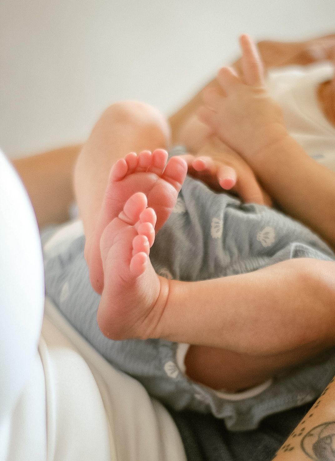 Close-up of baby feet in gray onesie while resting on white surface.