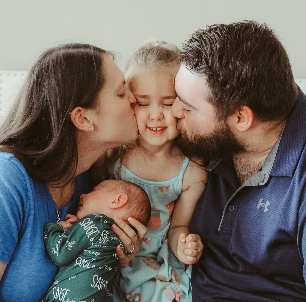 A loving family moment as parents kiss their young daughter while holding a newborn baby.
