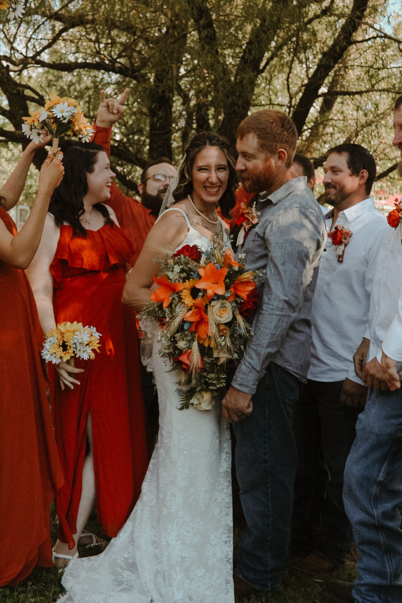 Wedding party celebrates outdoors with bridesmaids in vibrant red dresses and colorful autumn bouquets.