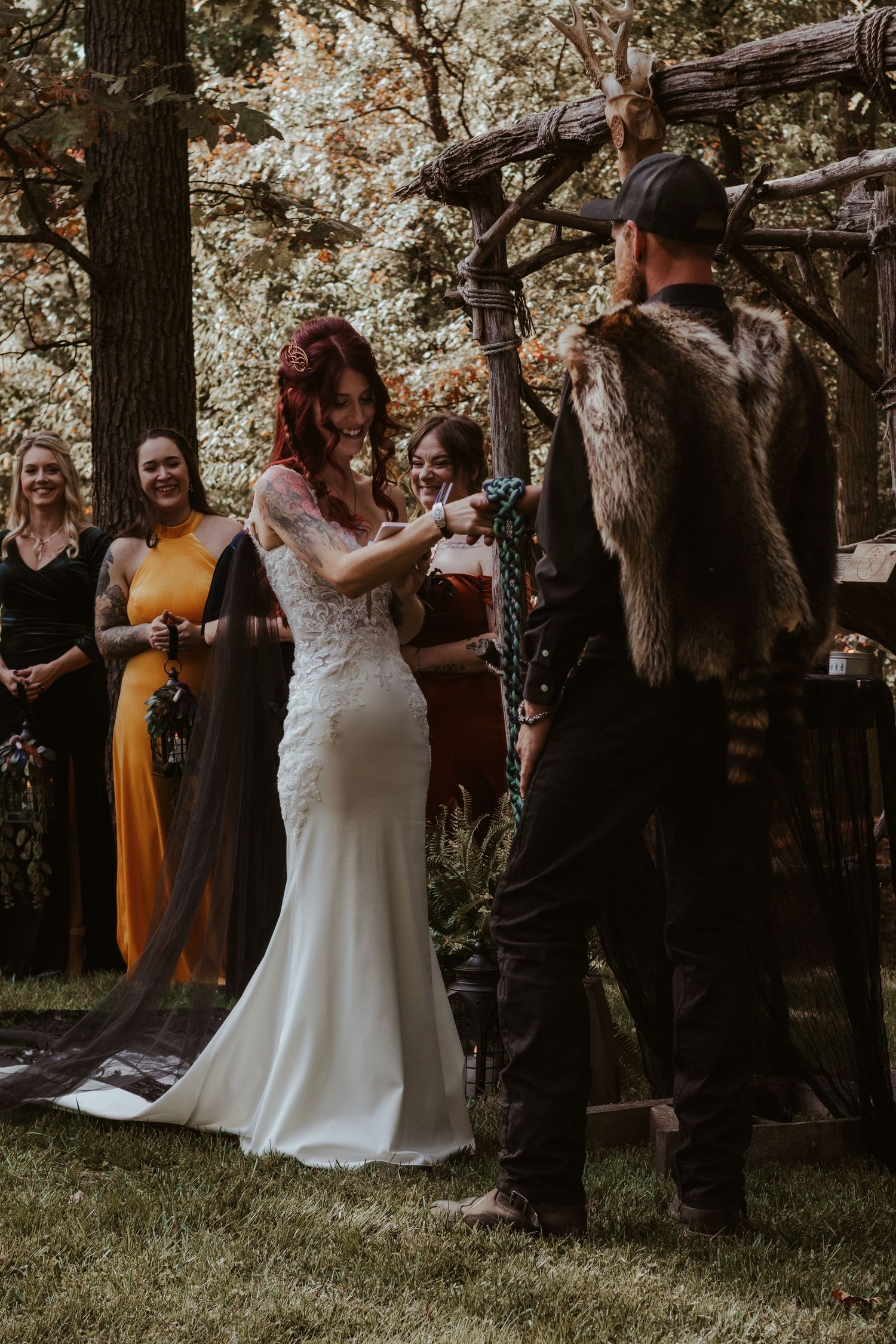 Wedding party gathers under trees in an outdoor autumn ceremony with guests in yellow dresses.