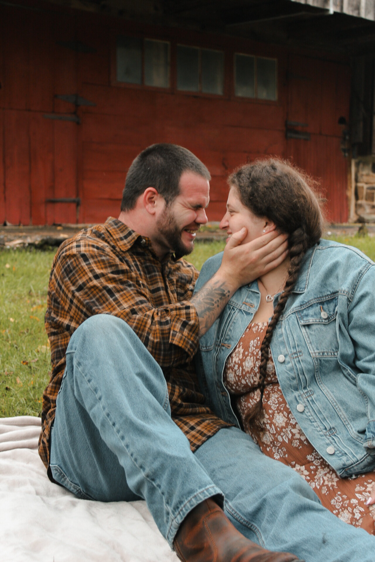 Couple sharing intimate moment on blanket outside rustic red barn.