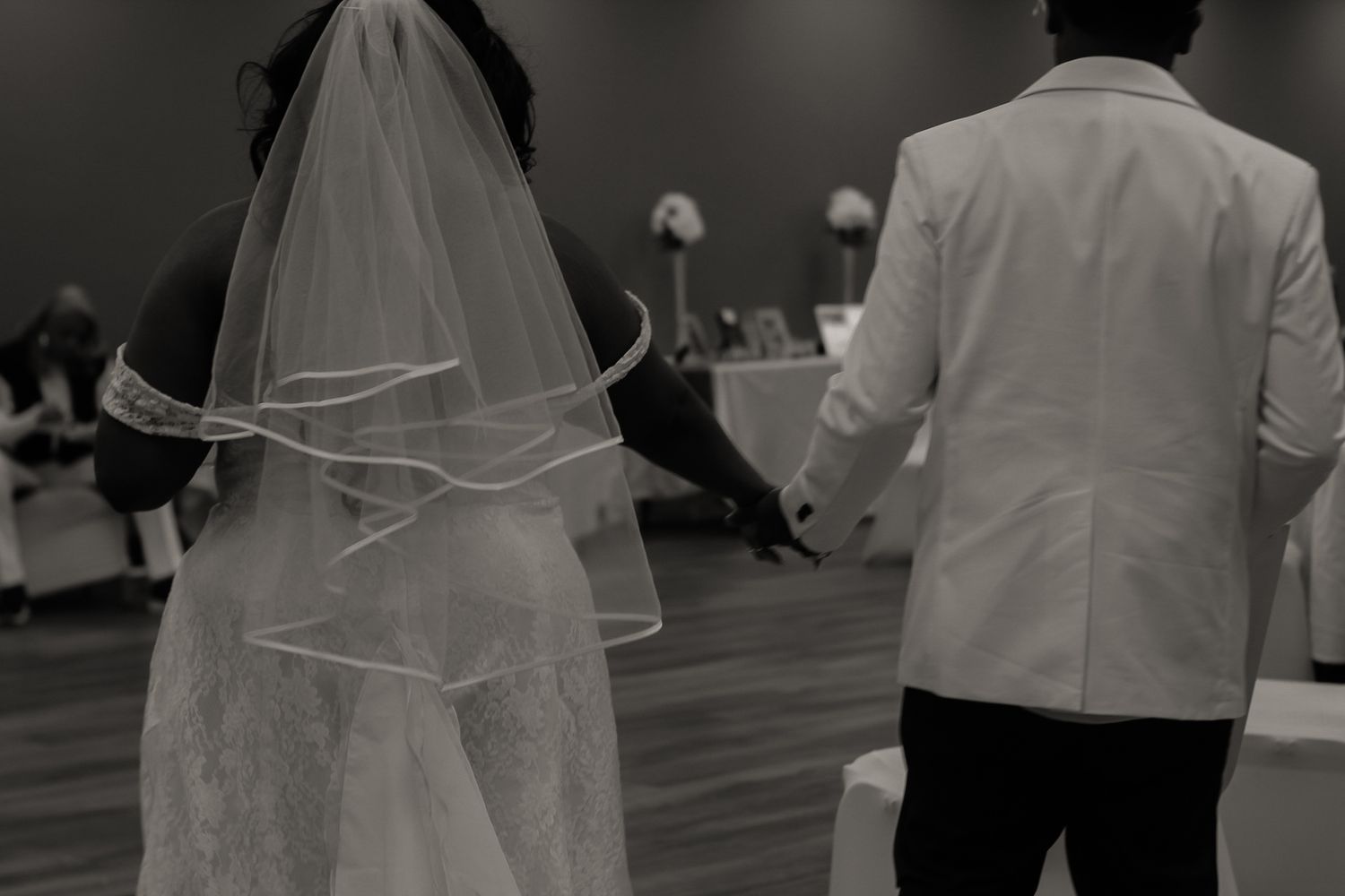 A black and white wedding photo captures dancing silhouettes on a hardwood floor.