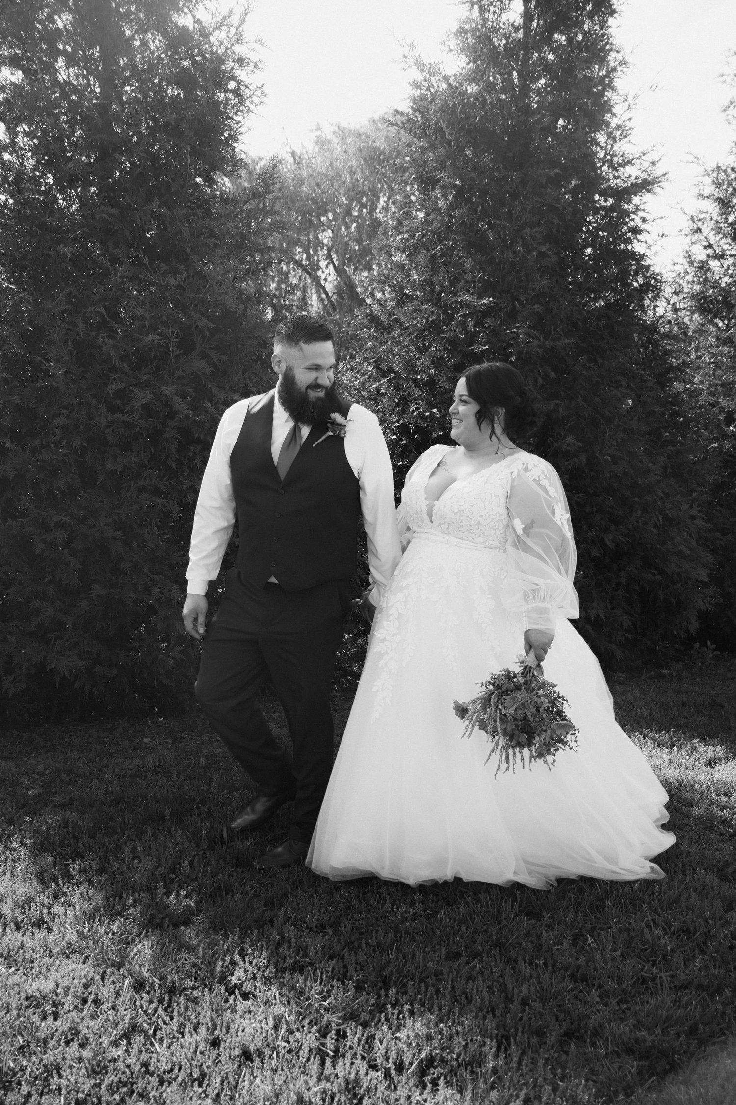 Black and white photo of bride and groom walking hand in hand outdoors on wedding day.