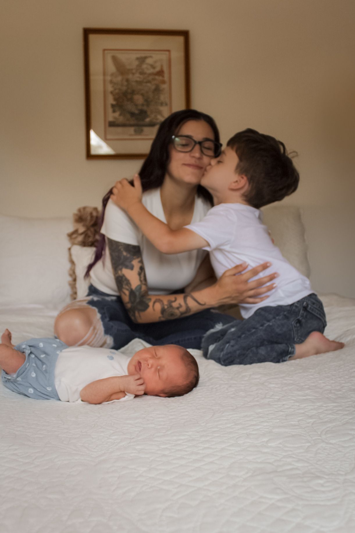 Intimate family moment captured on a comfortable white bed with decorative art displayed above.