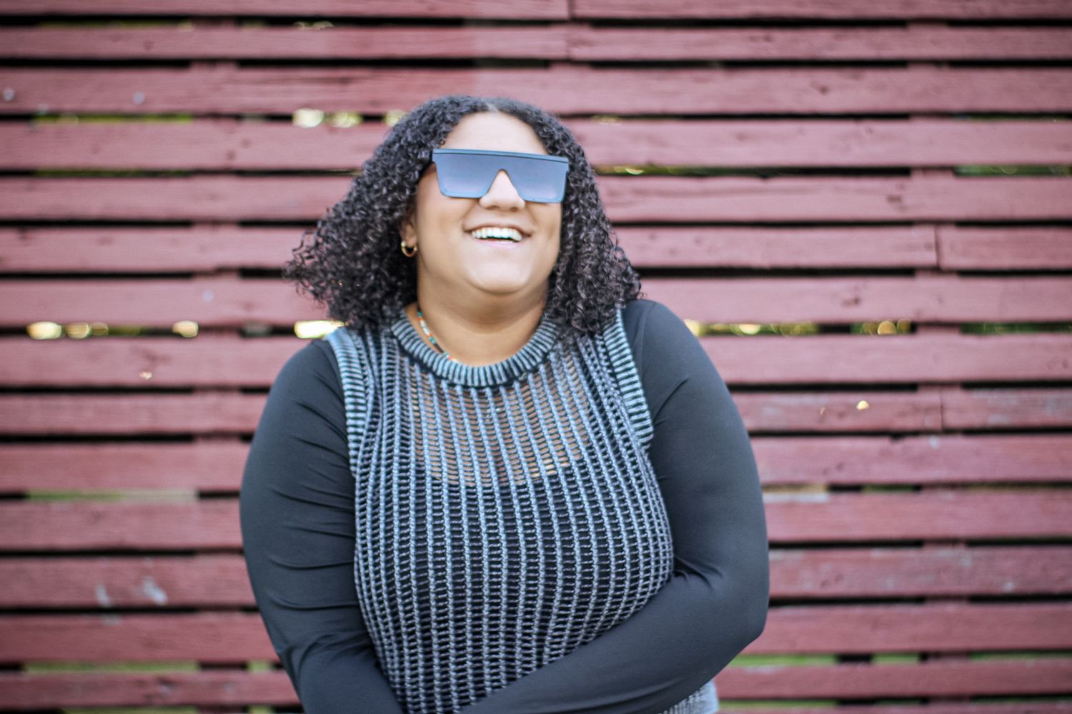Outdoor portrait against a pink wooden wall wearing a grey knit sweater and black top.