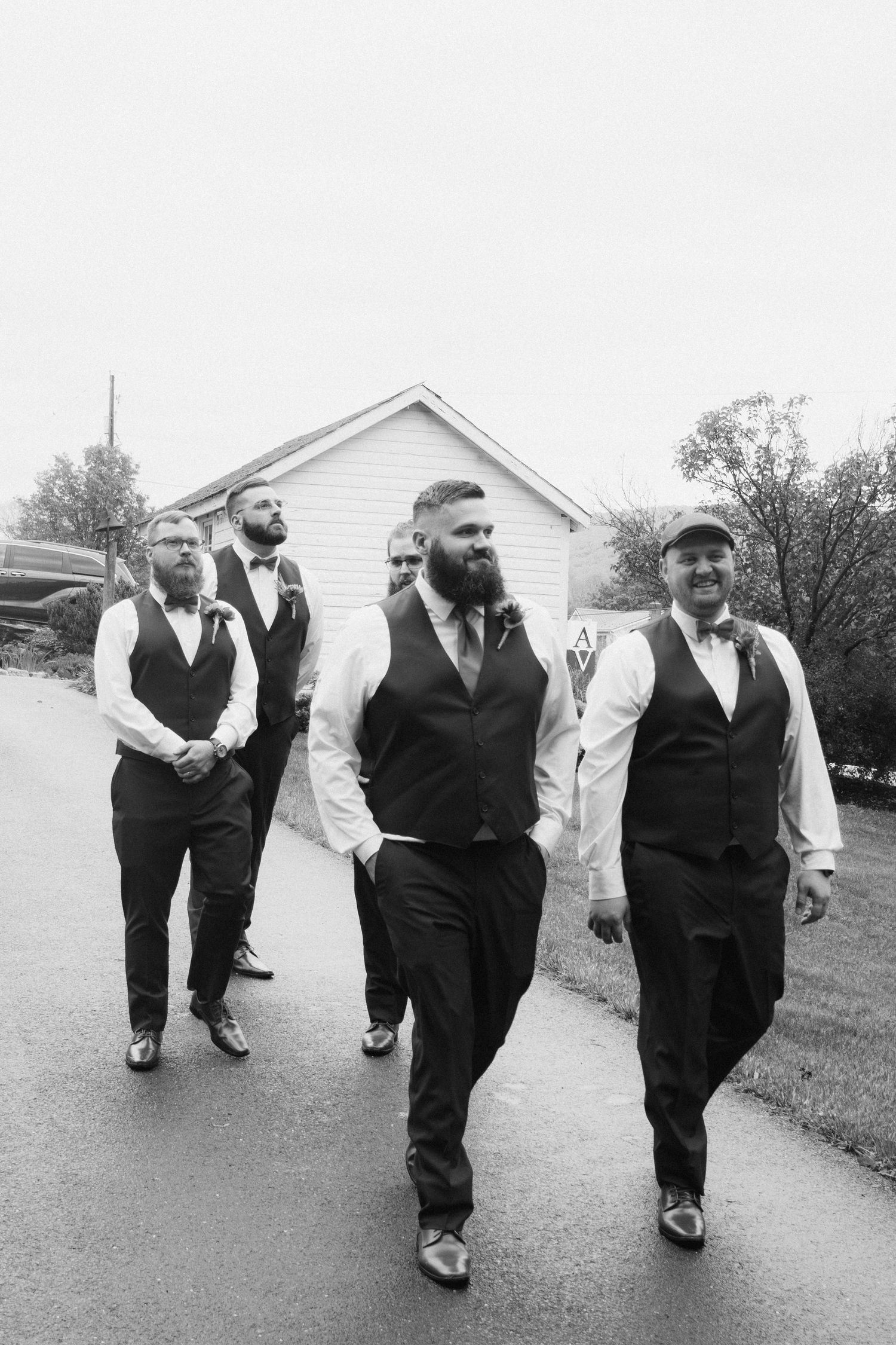 Groom and groomsmen walk confidently in matching vests and bow ties in black and white wedding photo.