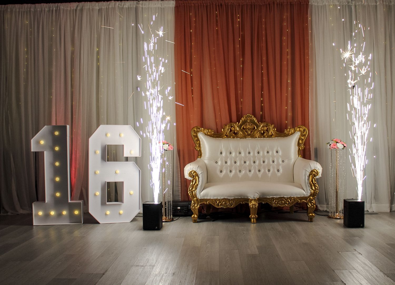 Elegant event setup with white sparkling fountains flanking an ornate throne chair against draped backdrop.