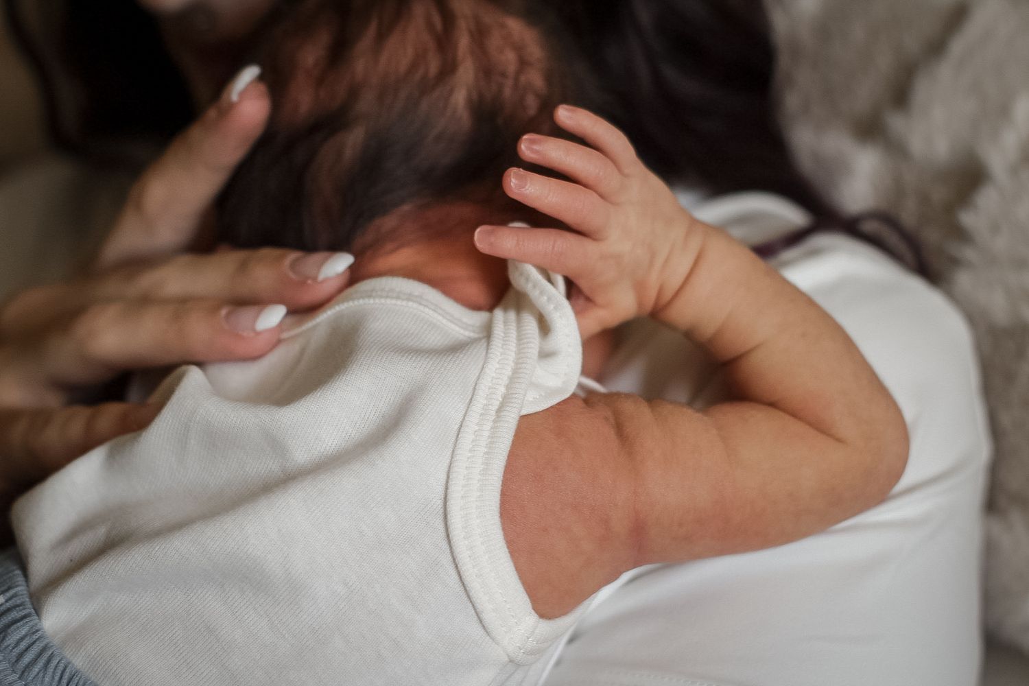 Tender moment showing hands gently cradling infant in white clothing.