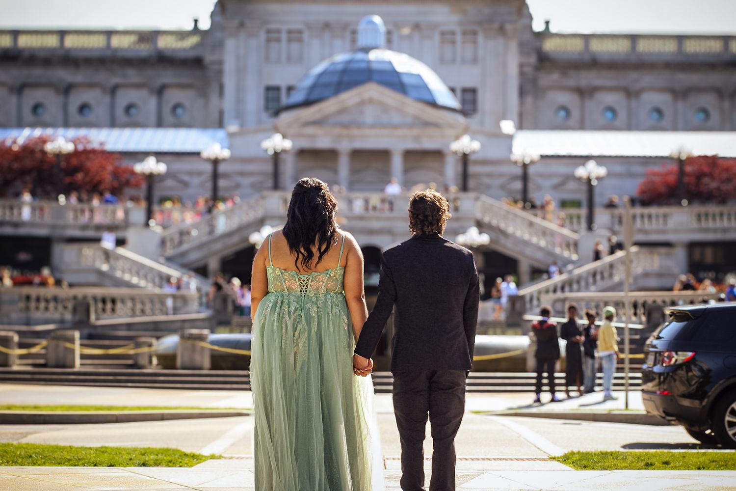 An elegant couple poses for portraits in front of a grand stone building.