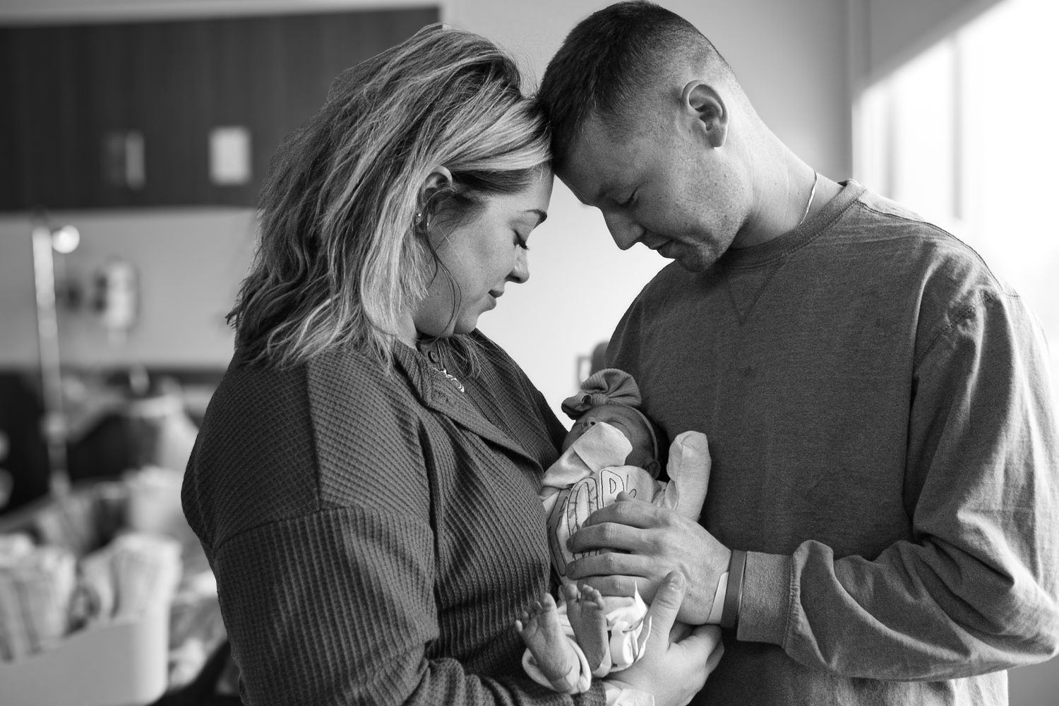 Intimate black and white portrait of parents admiring their newborn baby in a hospital setting.