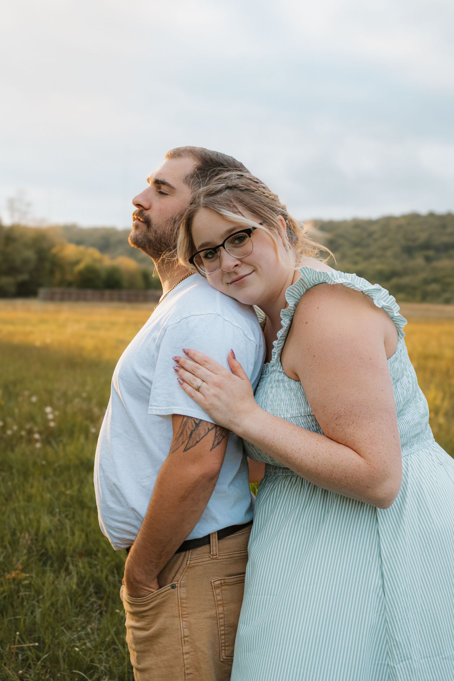 A woman in a mint dress hugs a bearded man from behind in a golden field during a couples outdoor photo session.
