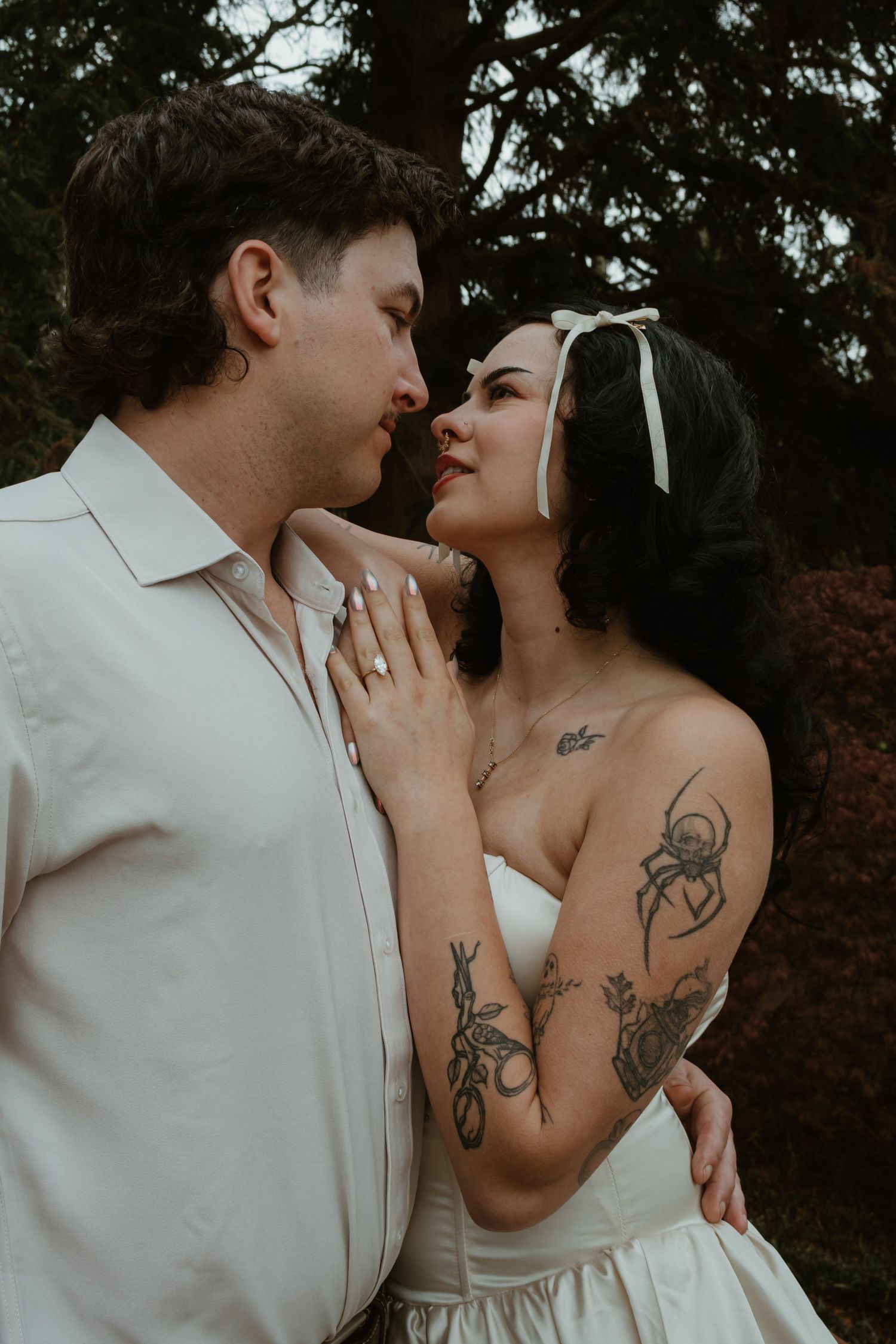 A tattooed bride in a white strapless gown and headband shares a romantic moment with her groom outdoors.