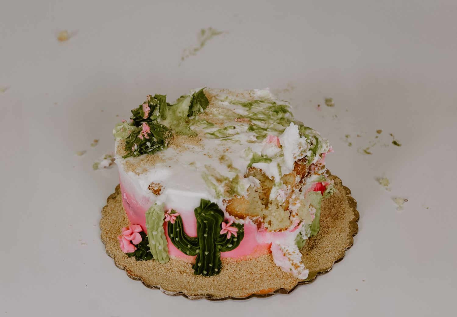 A destroyed birthday cake with green frosting and pink decorative elements on a gold base.