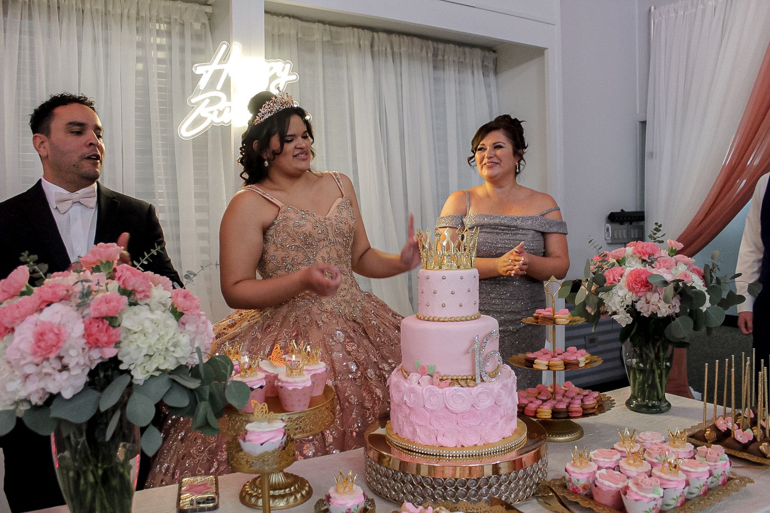 Festive celebration table adorned with pink cakes, floral arrangements and golden accents.