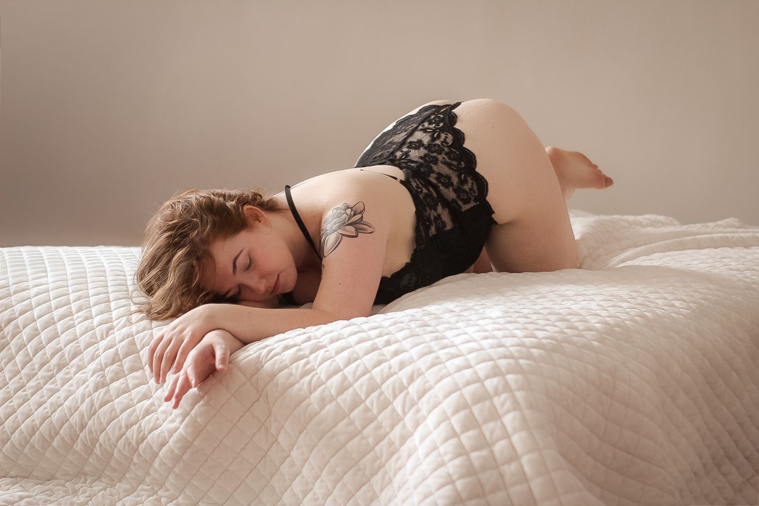 Intimate boudoir portrait on white quilted bedding with soft natural lighting.