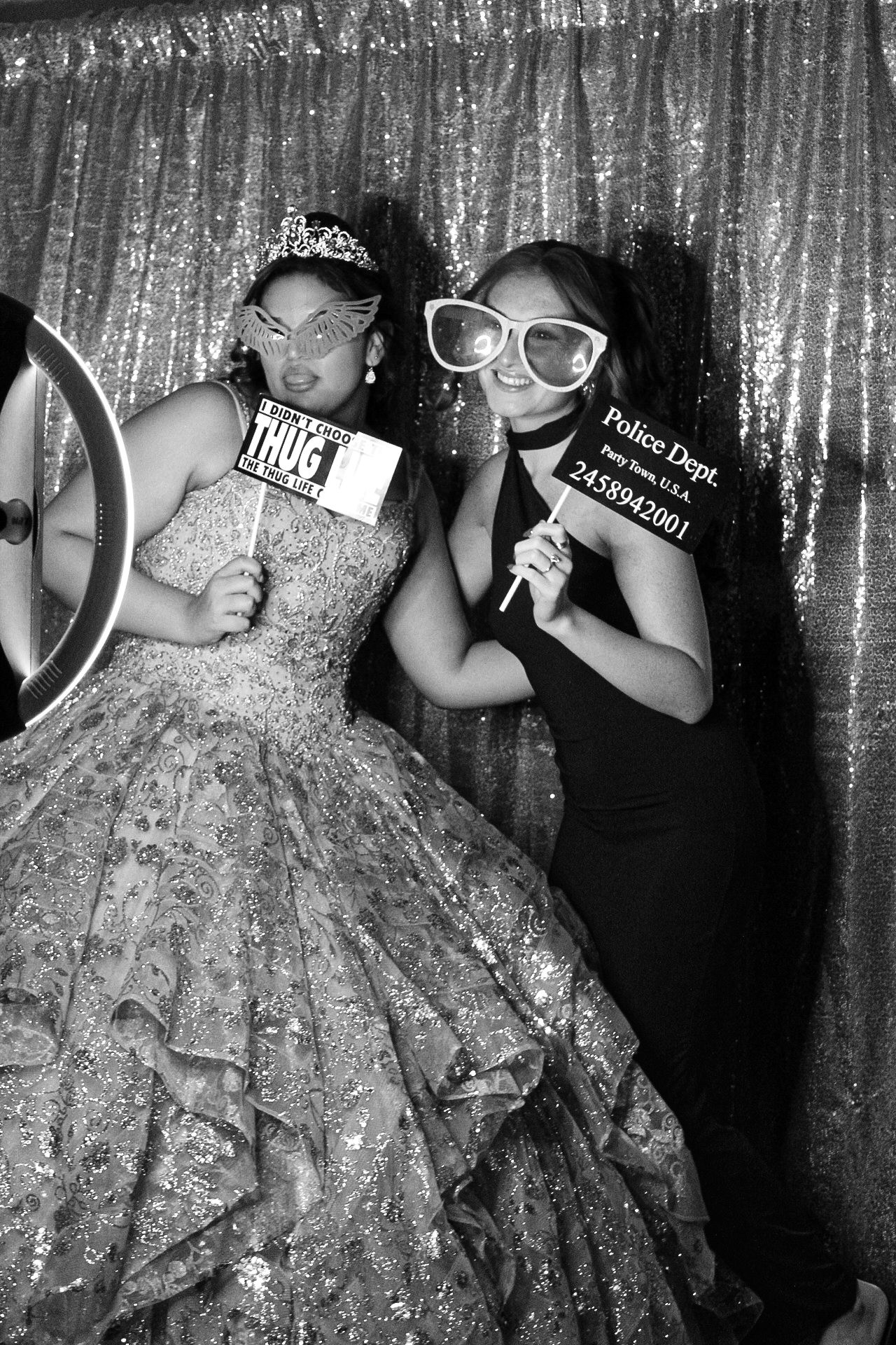 Two party guests pose playfully with photo booth props against a silver backdrop at a celebration.