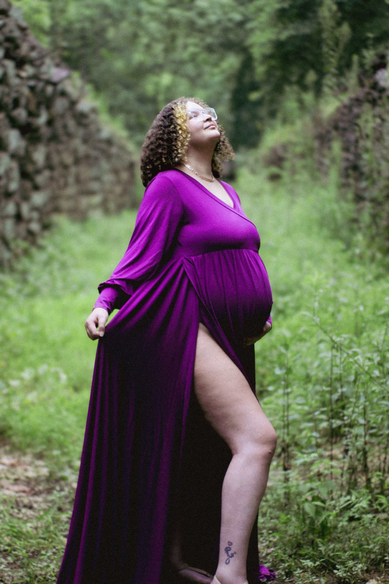 A maternity photo showing a pregnant woman in purple dress posing on a rustic path.