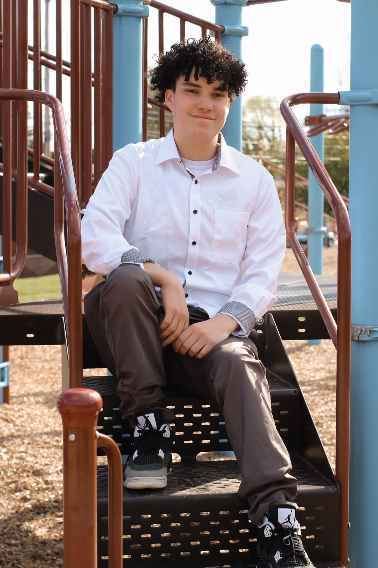 Senior portrait on playground equipment wearing white dress shirt and grey pants.