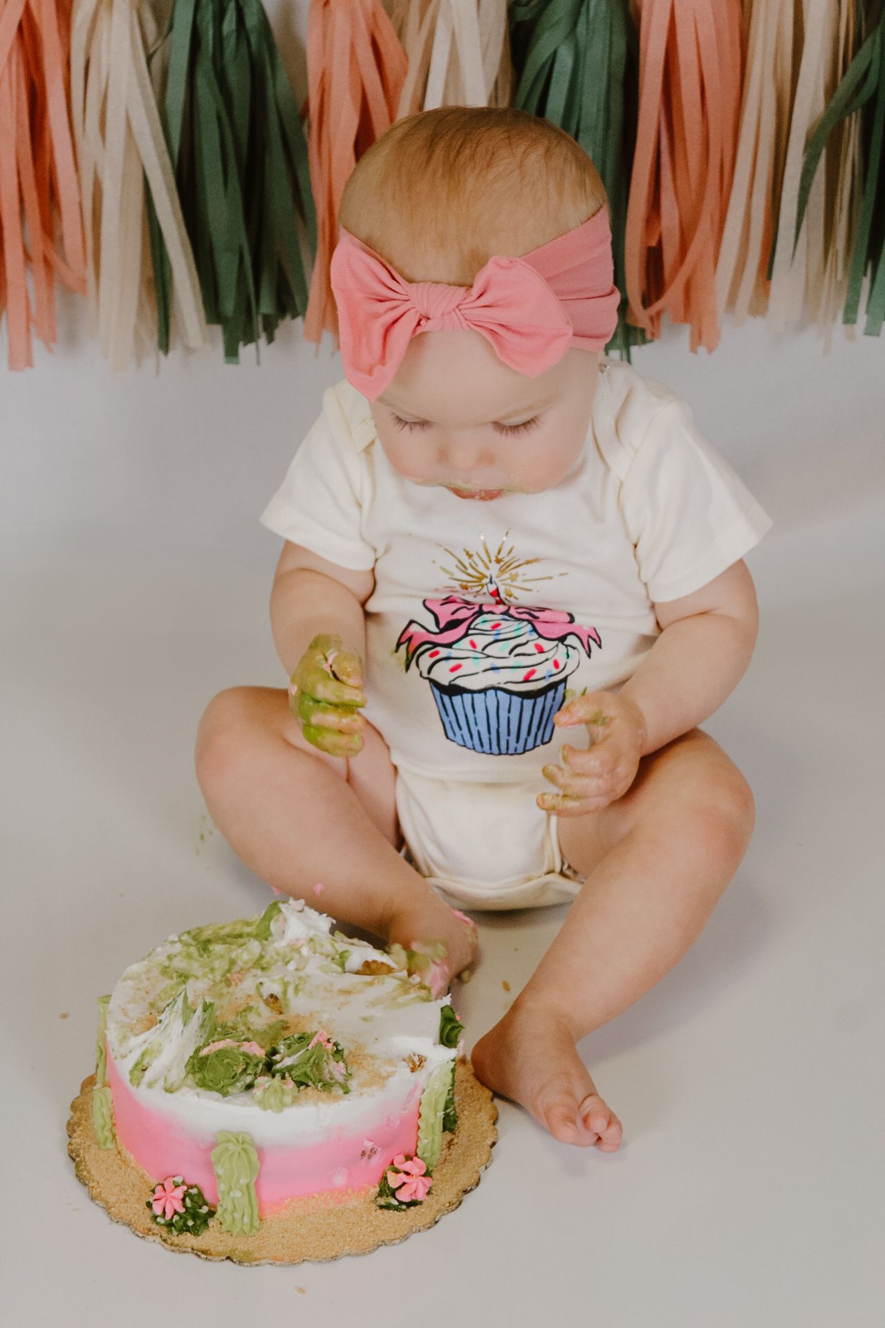 A cake smash photo with colorful tassels and a decorated cake against a white background.
