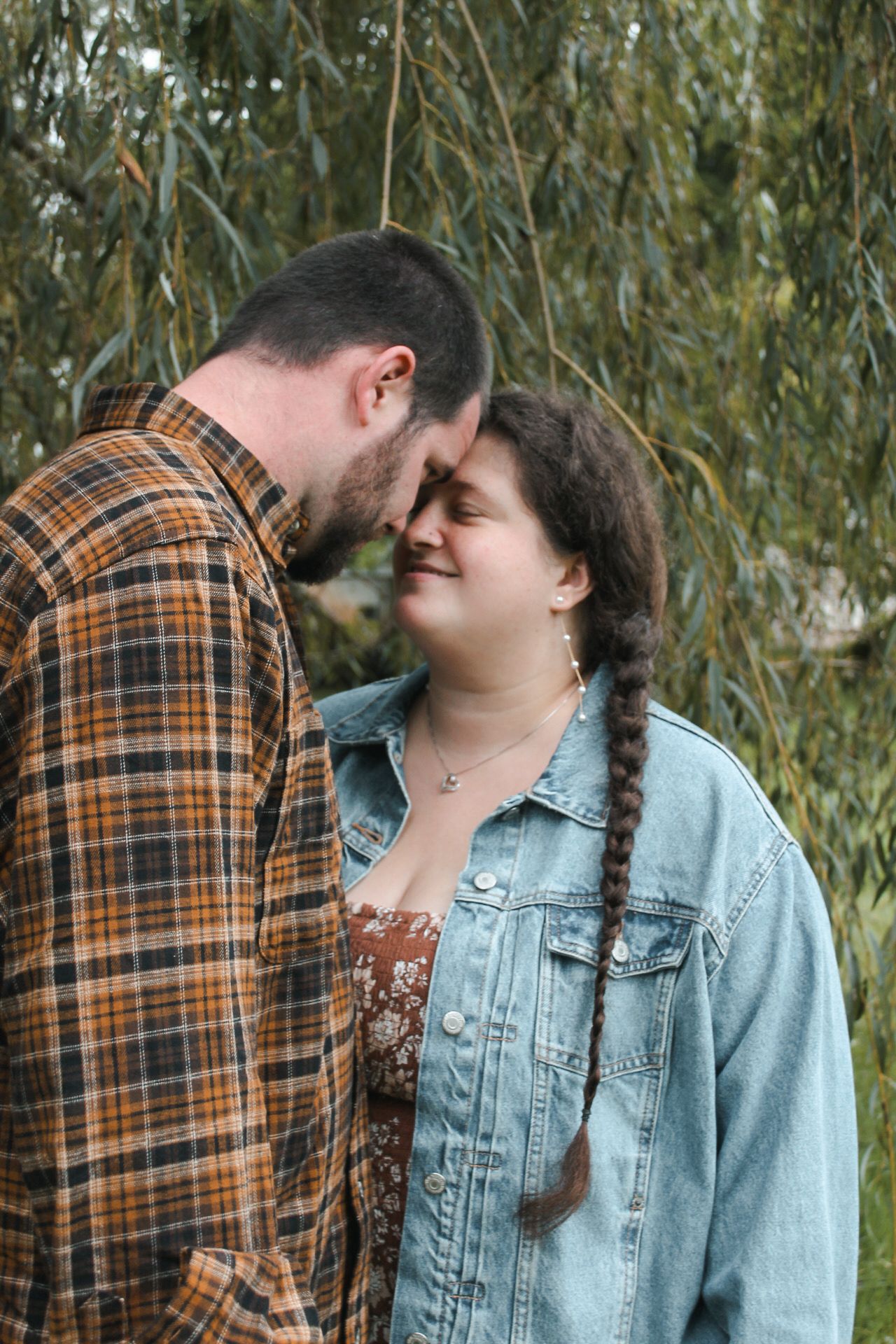 Romantic couple sharing intimate moment under willow tree branches.