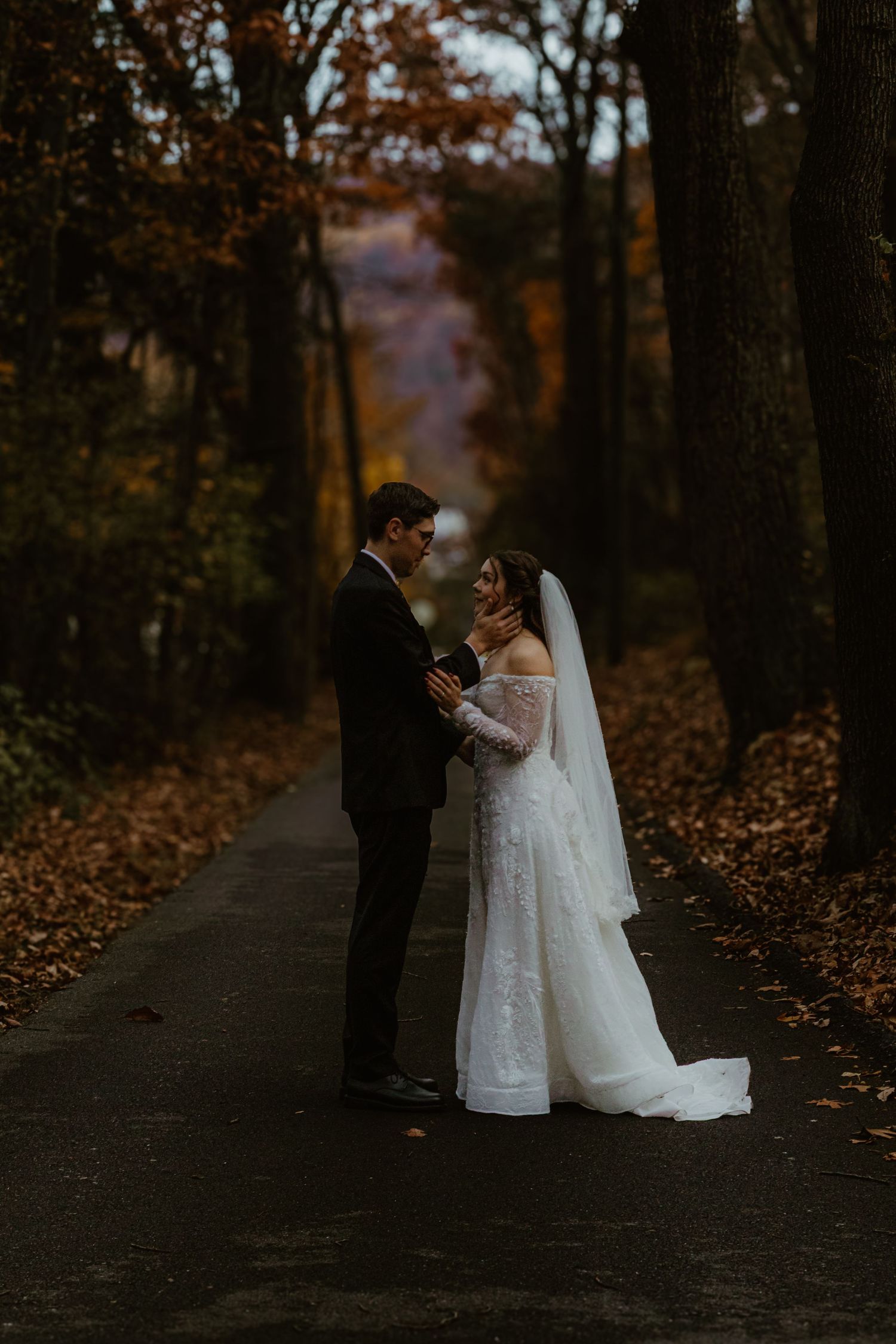 Couple shares intimate moments on a leaf-covered forest path during their autumn wedding photoshoot.