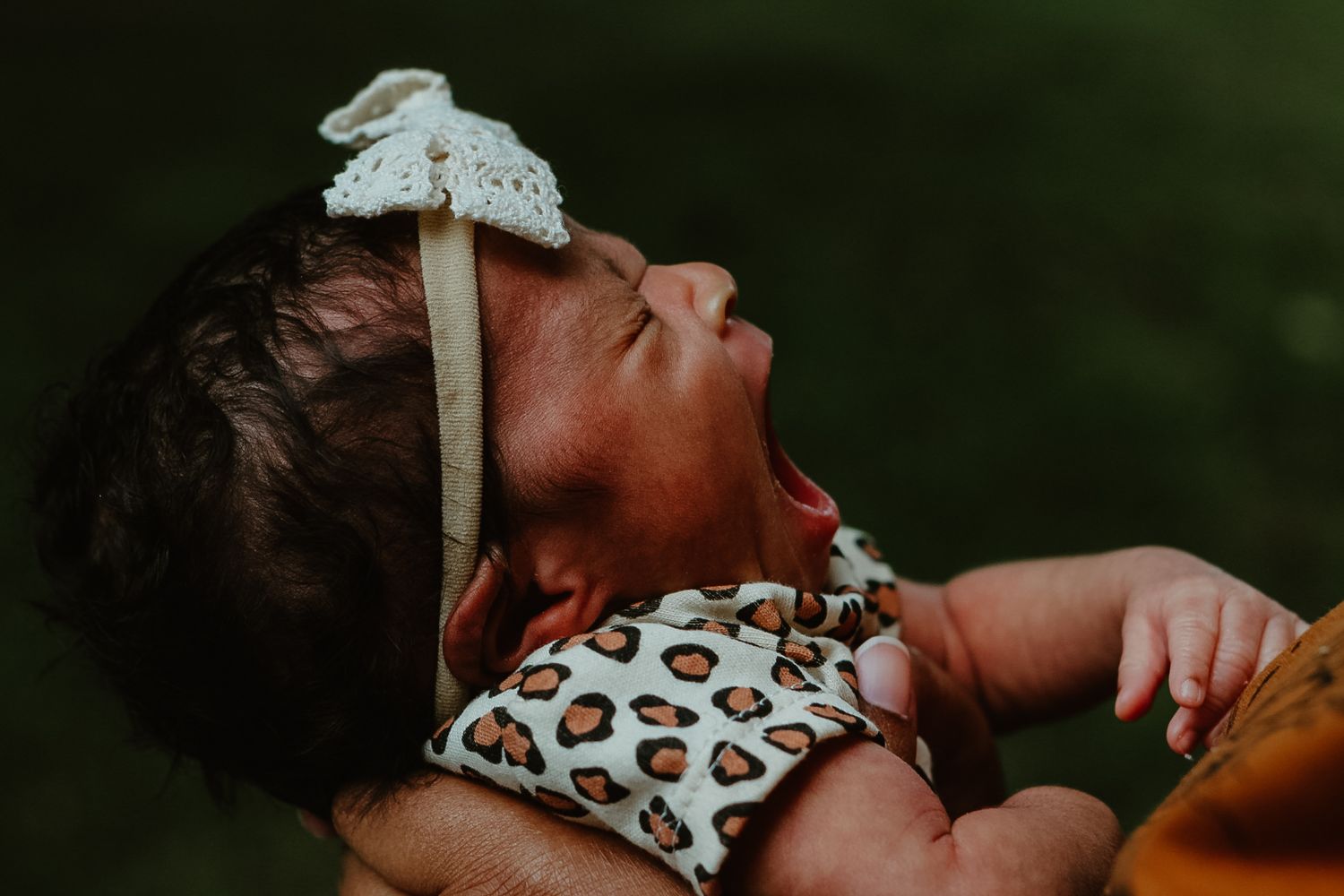Baby in leopard print onesie being held while yawning during a photoshoot.